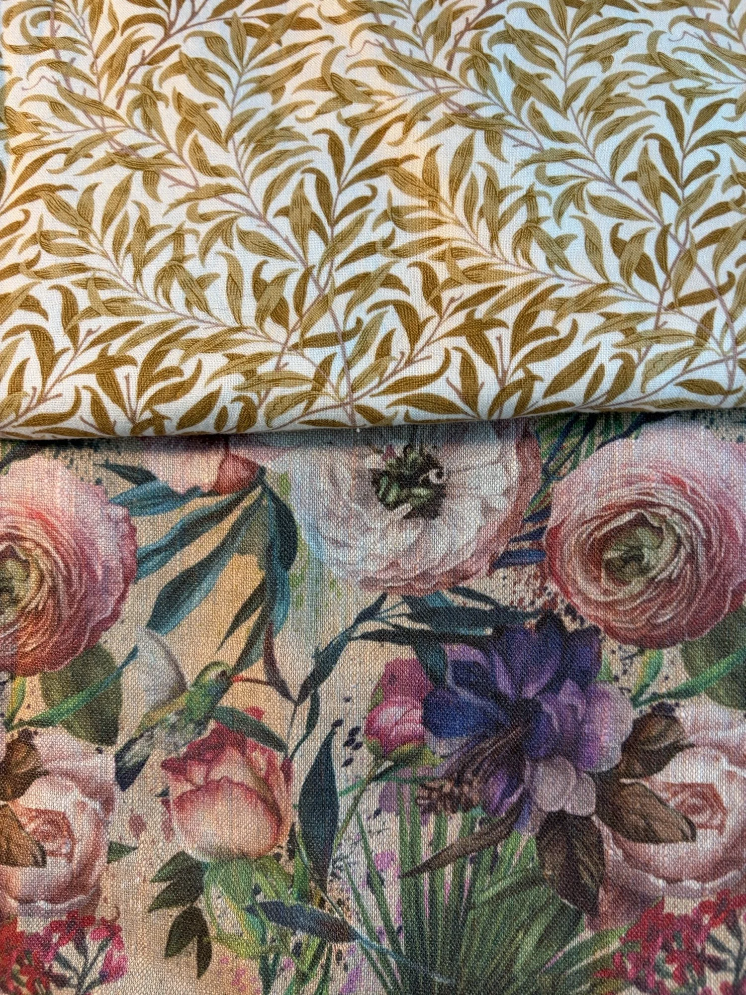 Close-up of layered floral fabrics featuring a brown leafy botanical print above colorful roses, irises, and other flowers.