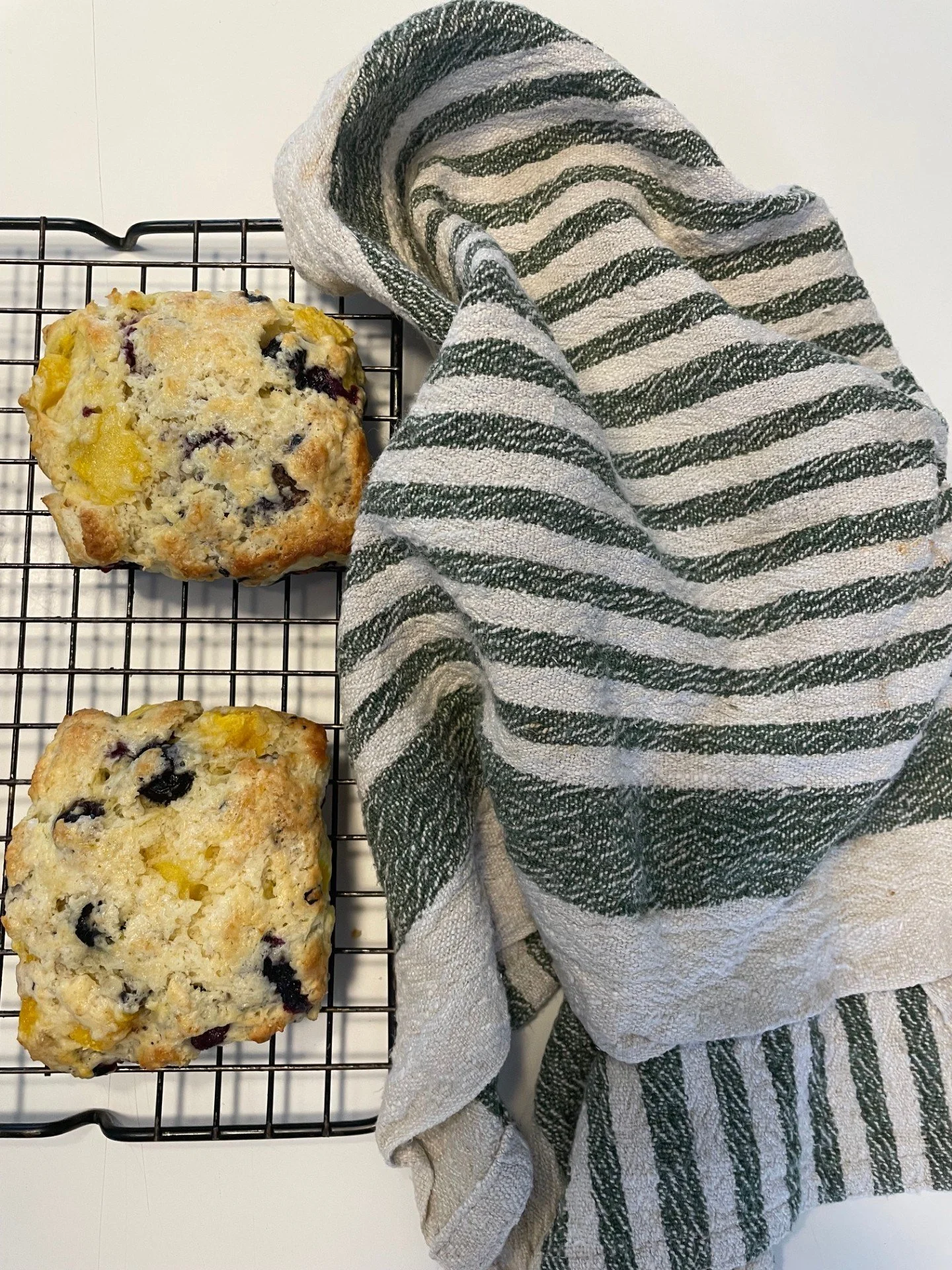 A green striped kitchen towel draped over scones cooling on a wire rack.