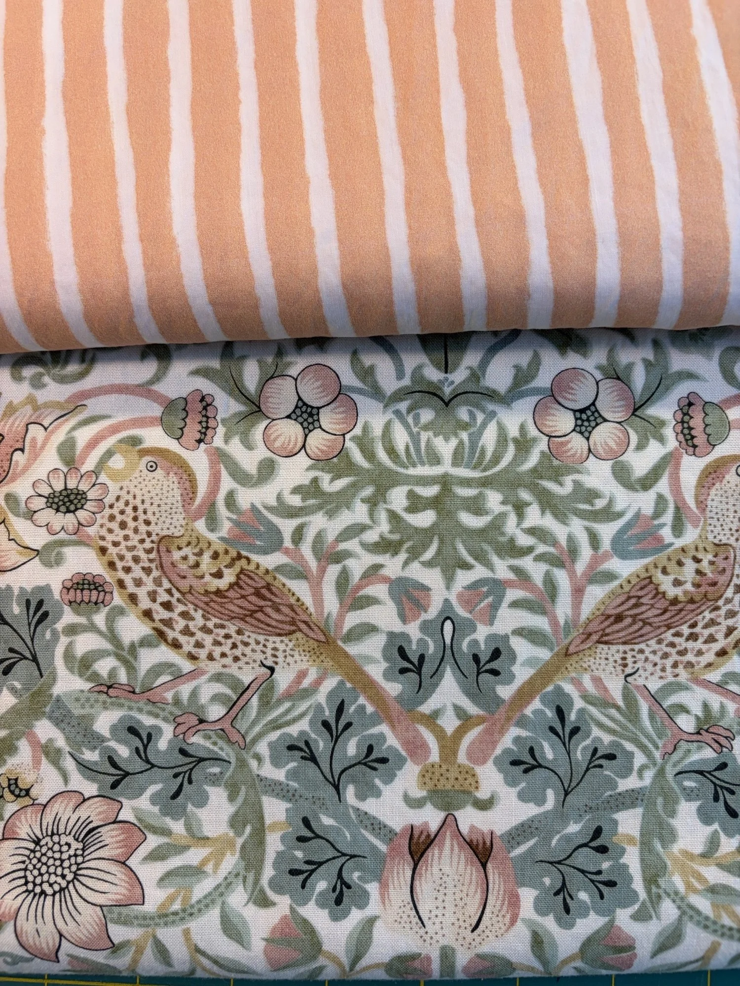 Close-up of vintage floral fabric featuring two birds, flowers, and leafy vines beneath orange-and-white striped fabric