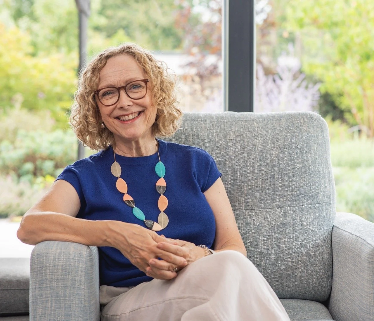 Juliet wearing glasses and a blue shirt sitting on a couch.