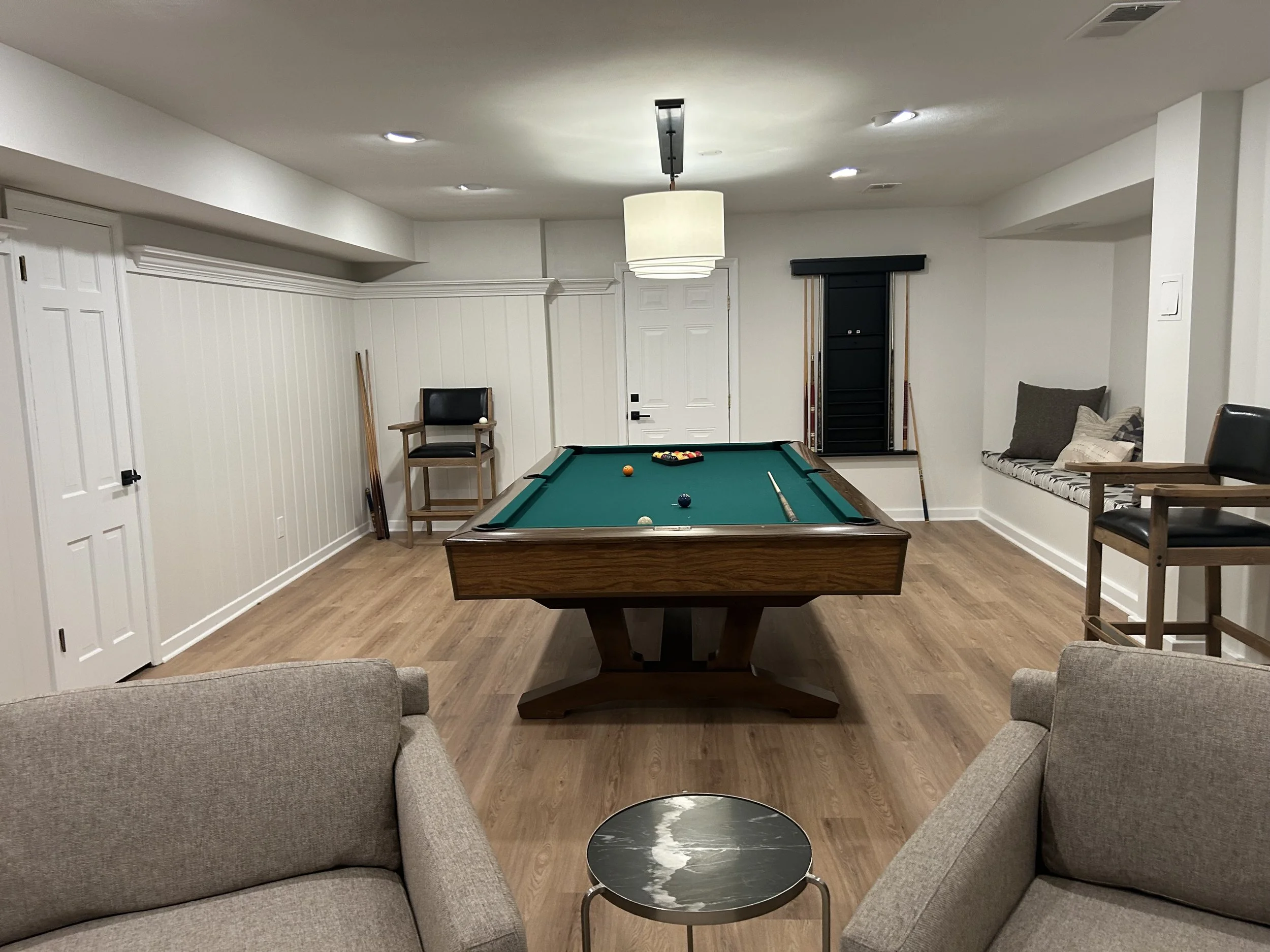 Indoor recreational room with a pool table, seating area with cushioned window seat, and wooden chairs.