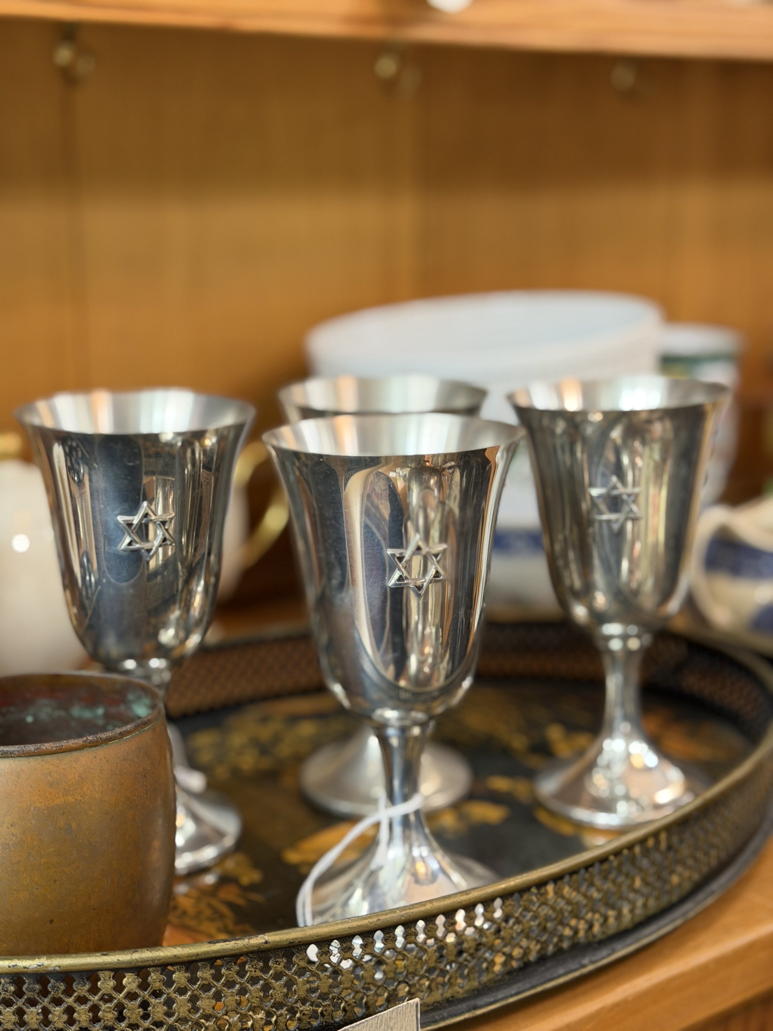 Three silver Kiddush cups with Star of David engravings on a decorative tray.
