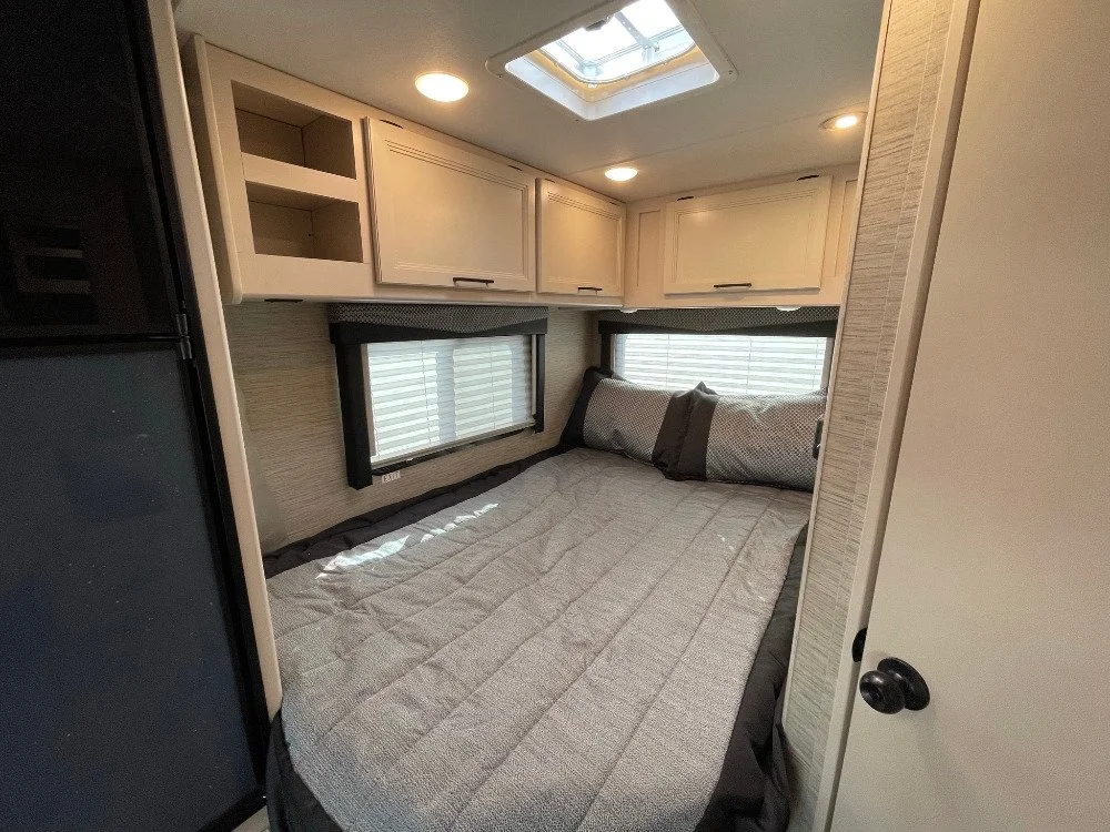 A cozy bedroom with a bed, pillows, overhead cabinets, and a skylight window in an RV or tiny home.