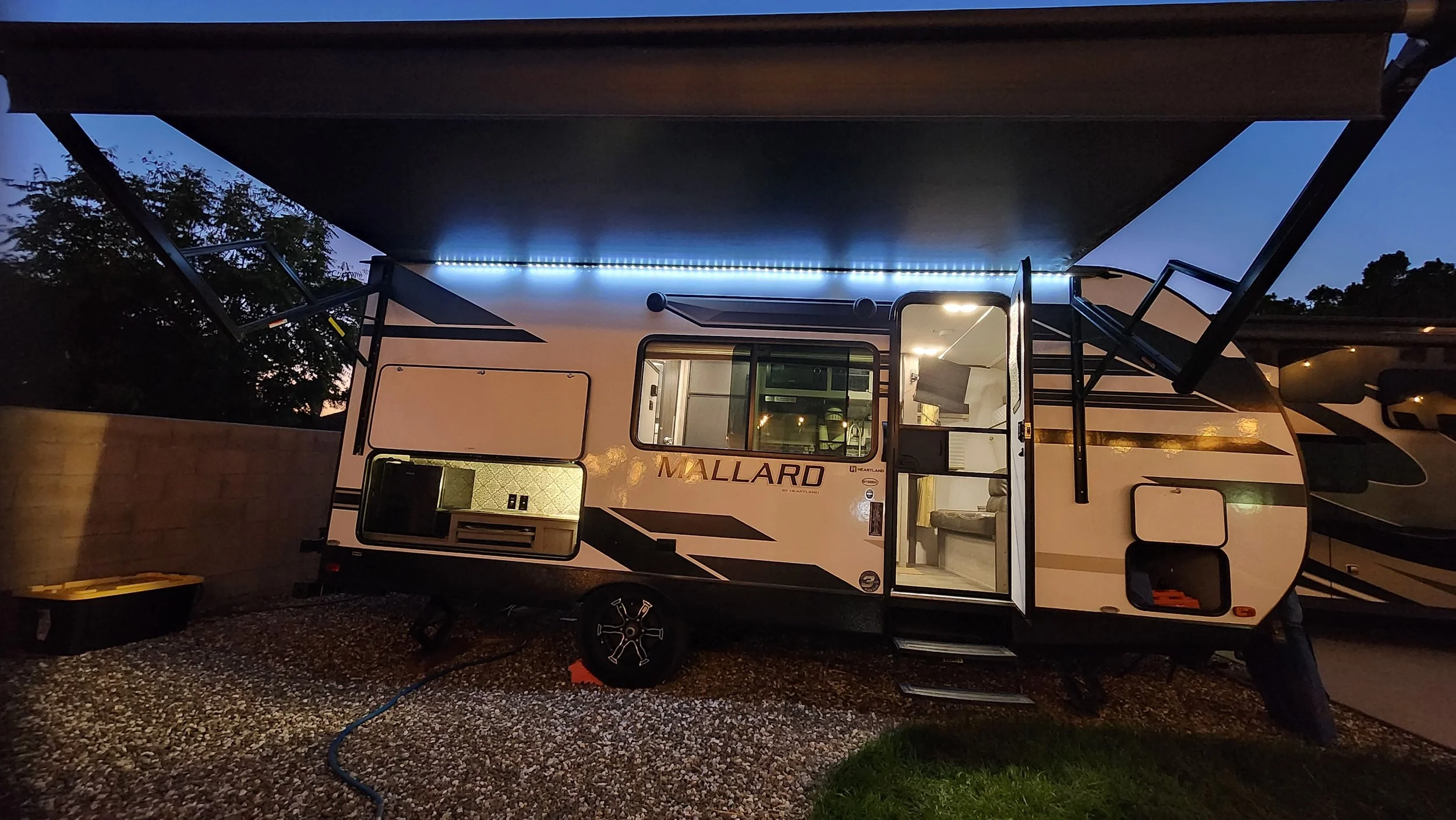 Travel trailer parked outdoors during dusk, with open door and interior lights on.