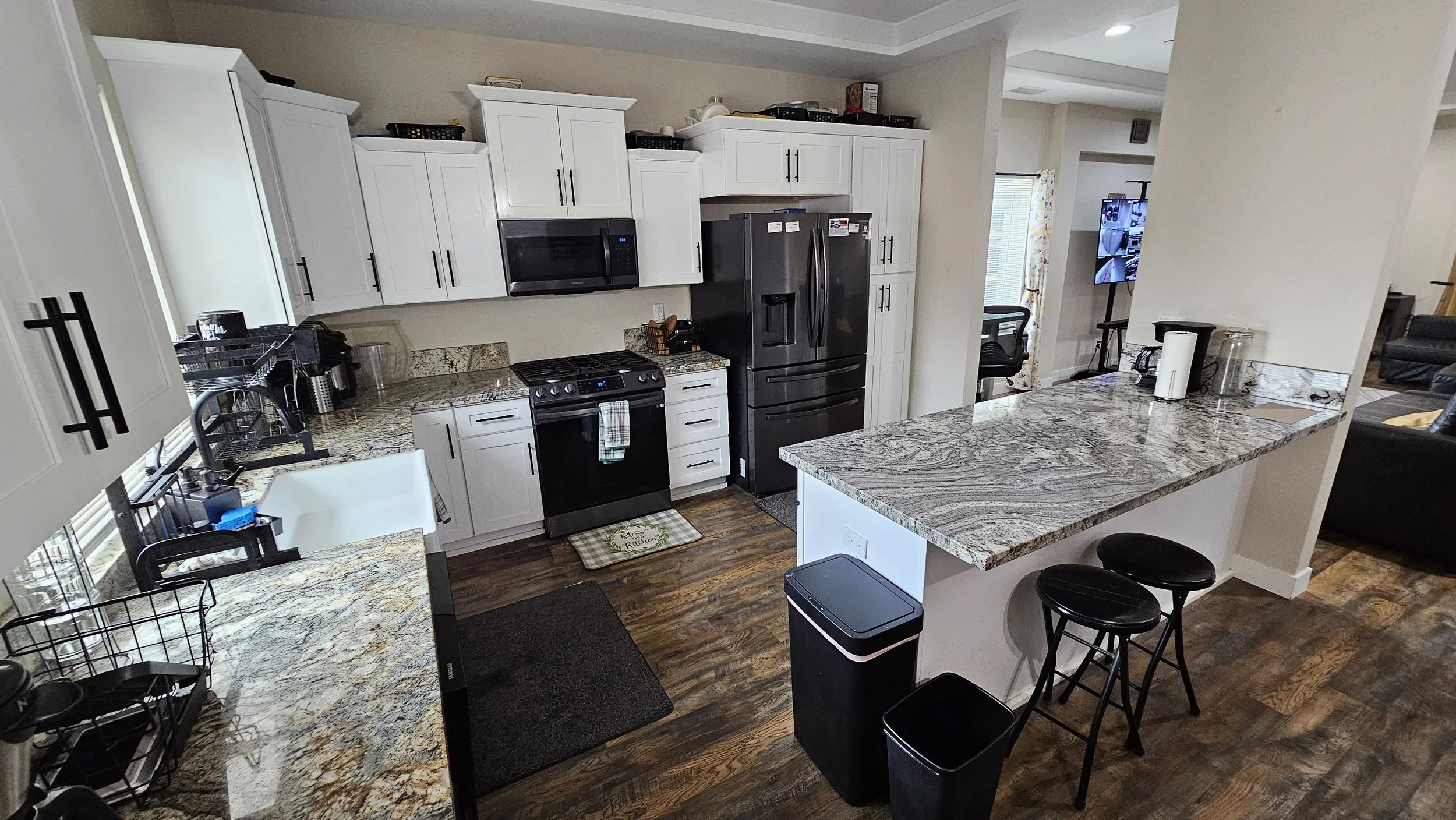 Kitchen with white cabinets, granite countertops, black appliances, and a small breakfast bar with two black stools.