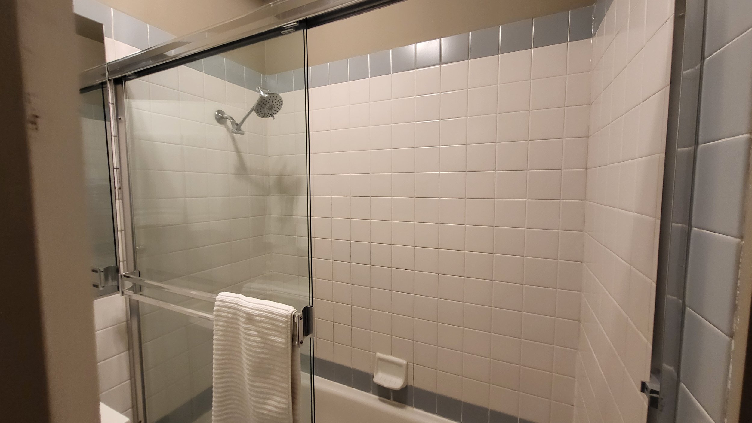 Bathroom shower with glass doors, a showerhead, and beige tiles on the wall.