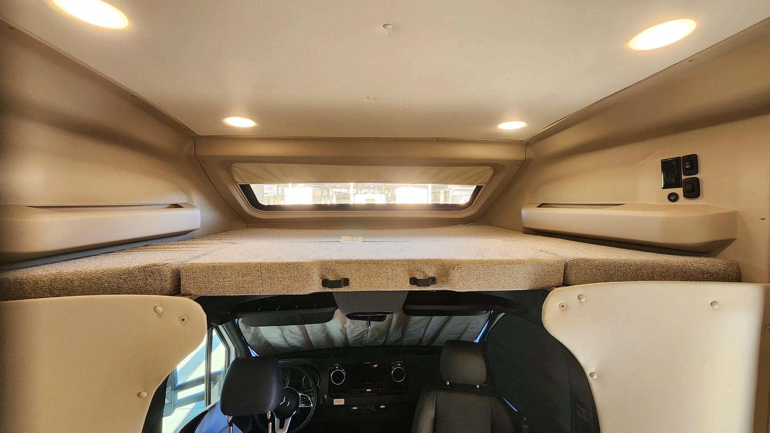 Interior of an RV with a sleeping area overhead, featuring a window and beige interior walls.