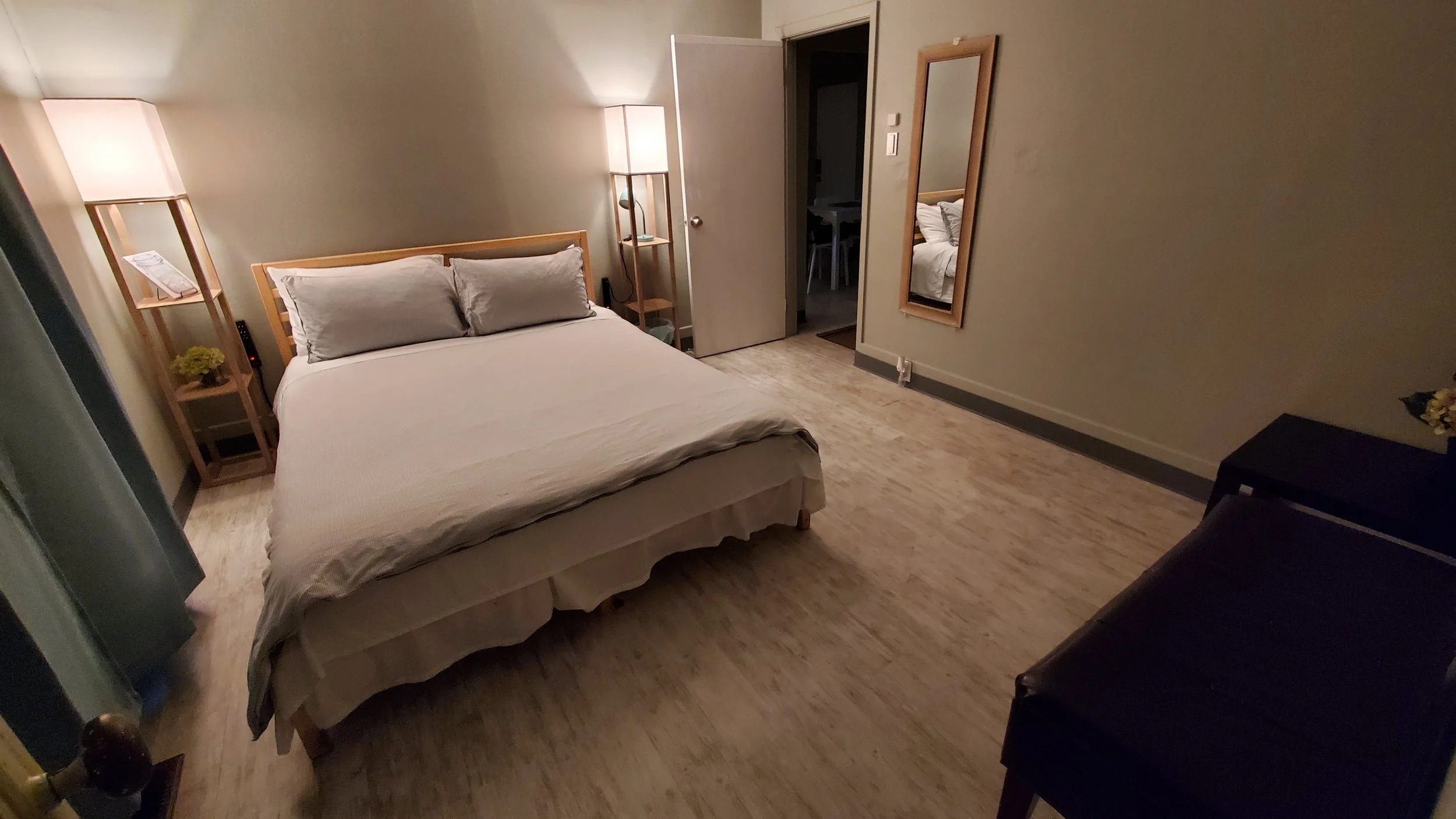 A bedroom with a bed, nightstands, lamps, mirror, and a small black table.