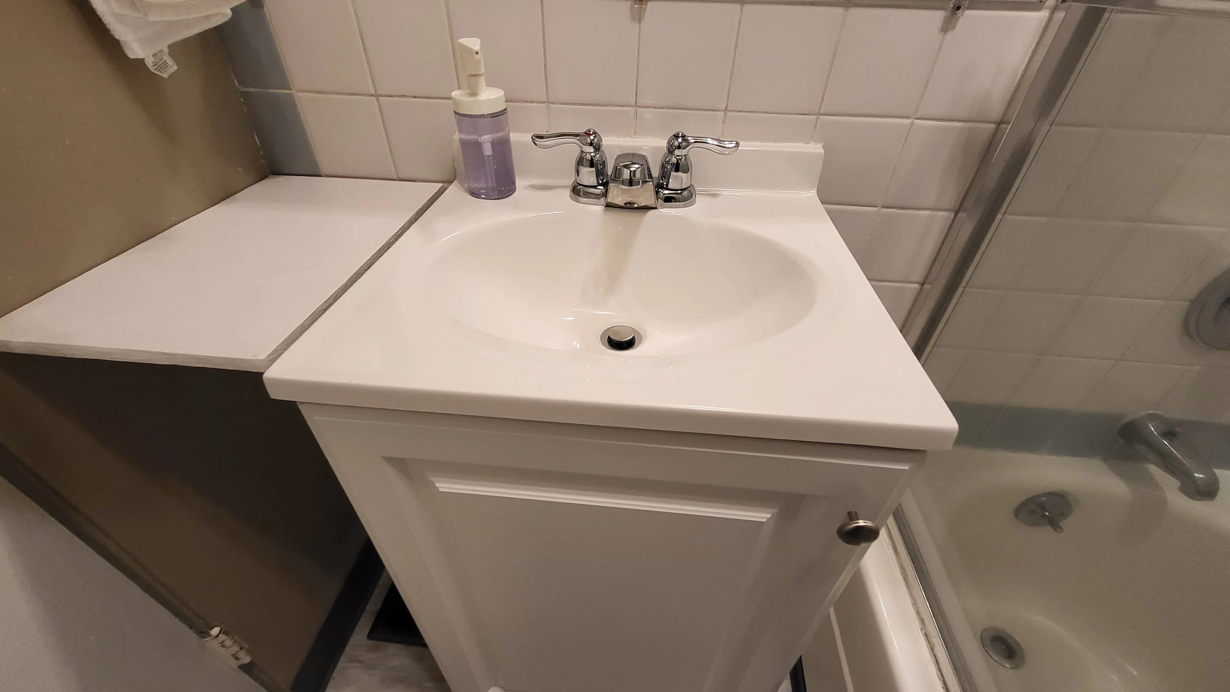 Bathroom sink with a soap dispenser on the left and a mirror above, part of a shower with a glass door on the right.