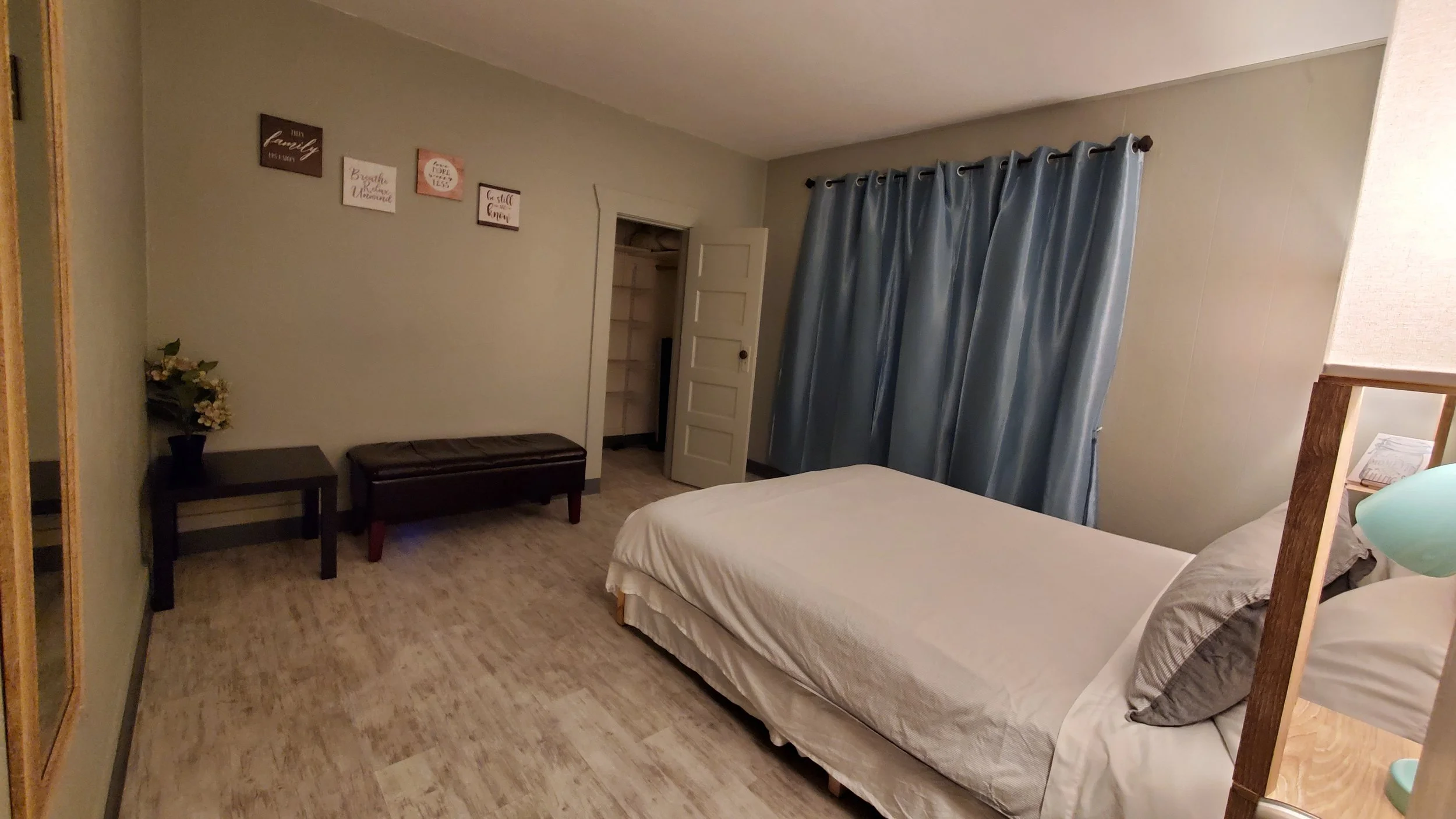 A bedroom with a bed, blue curtains, and wall art.