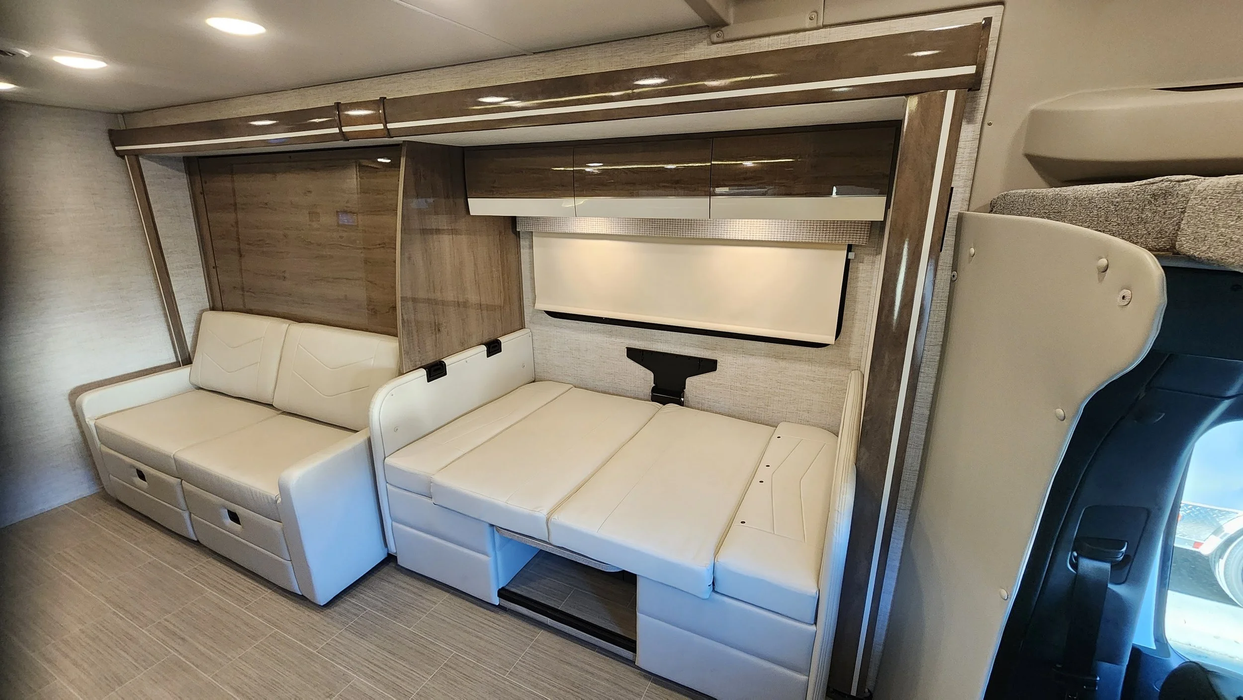 Interior of a recreational vehicle with white leather seating and a window with a beige shade.