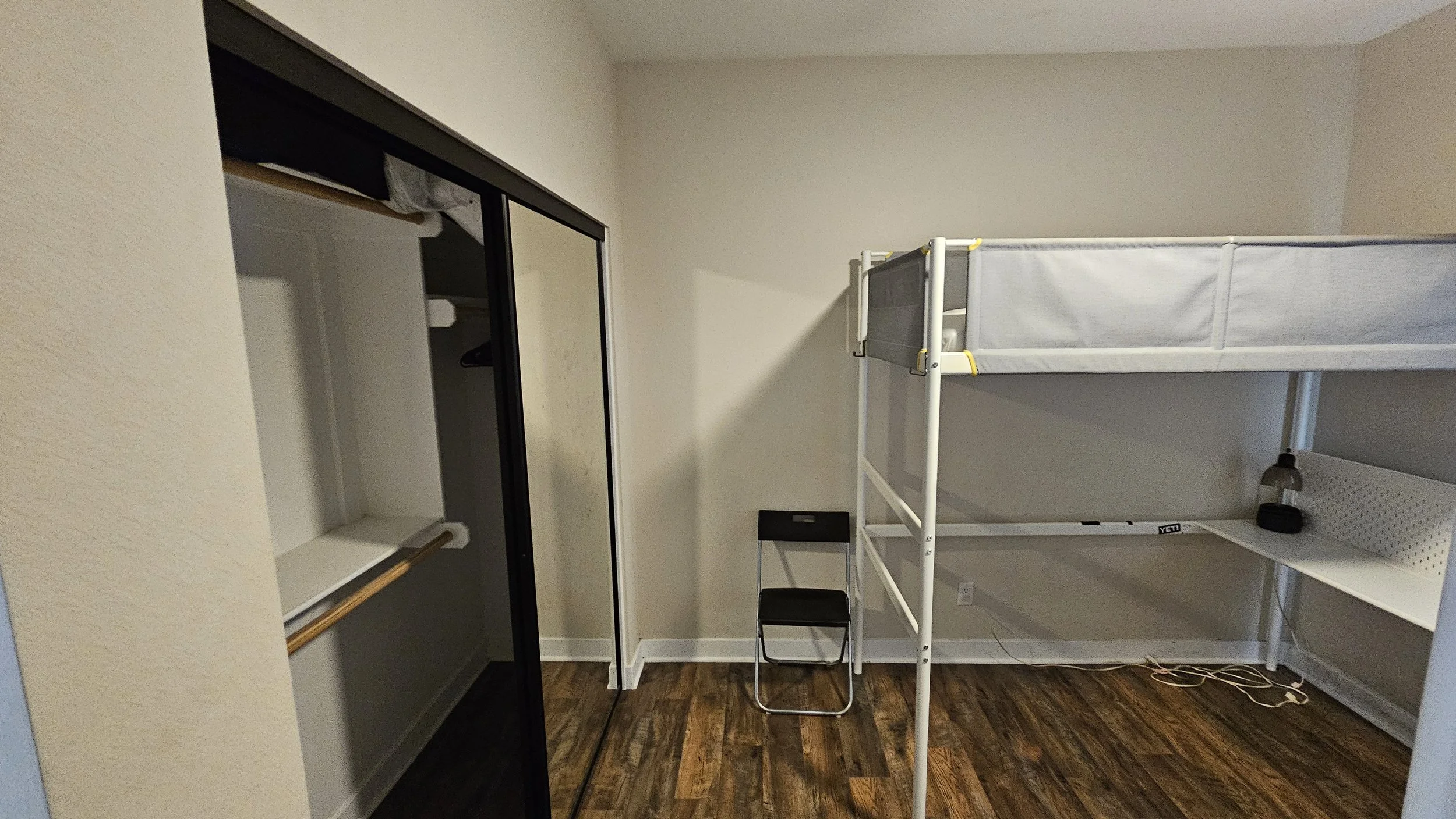 Empty room with a small desk, a bunk bed, and an open closet with sliding mirror doors.