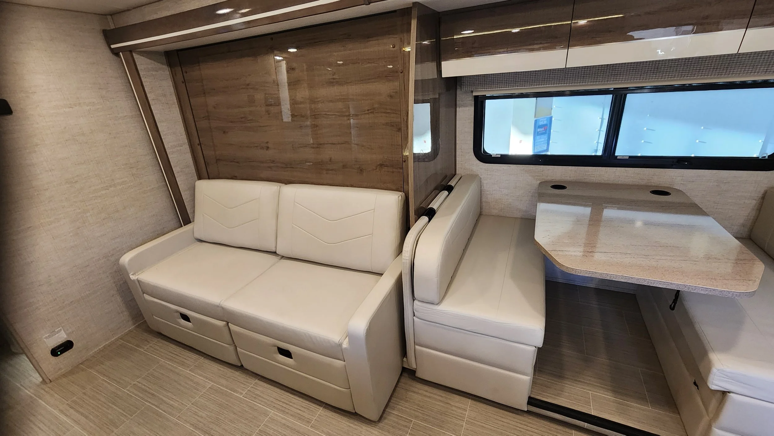 Interior of a modern RV with cream leather seating, a small dining table, and a window.