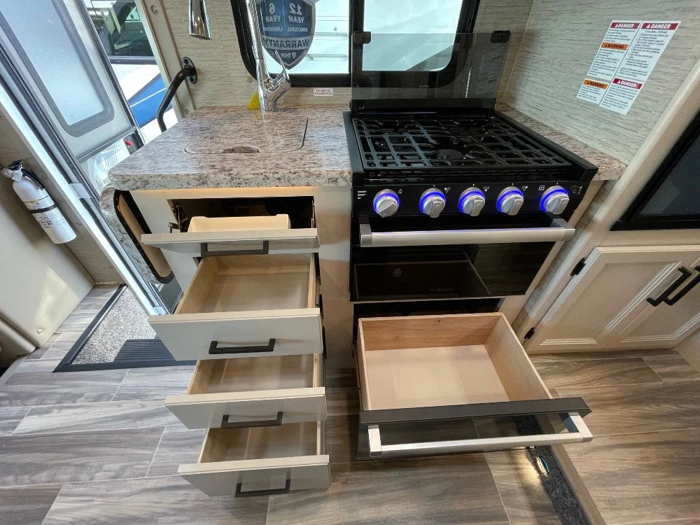 Kitchen countertop with sink, stove with knobs, open and empty drawers and cabinet in a small kitchen area.