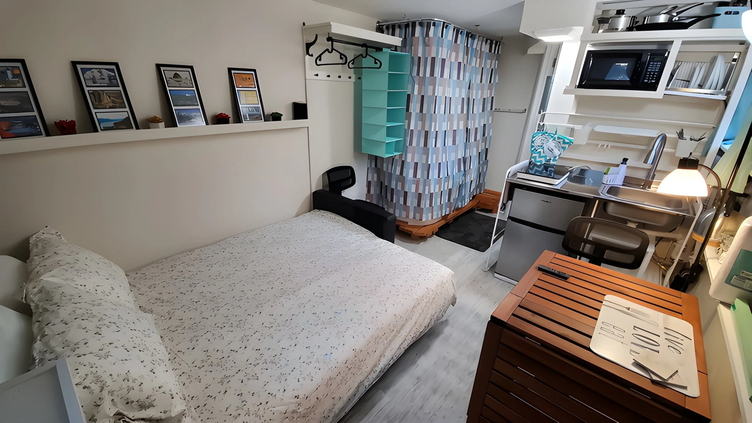 Small studio apartment with a bed, desk, kitchen area, and various storage units.