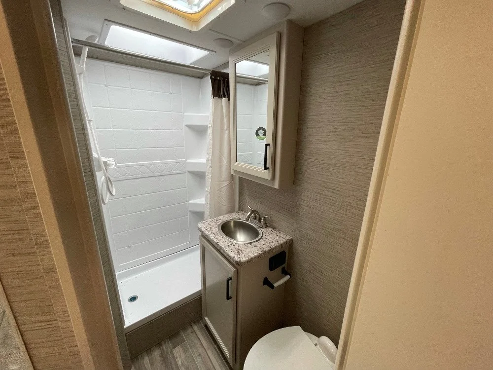 Small bathroom with shower, mirror cabinet, sink with granite countertop, and toilet, in a compact space.