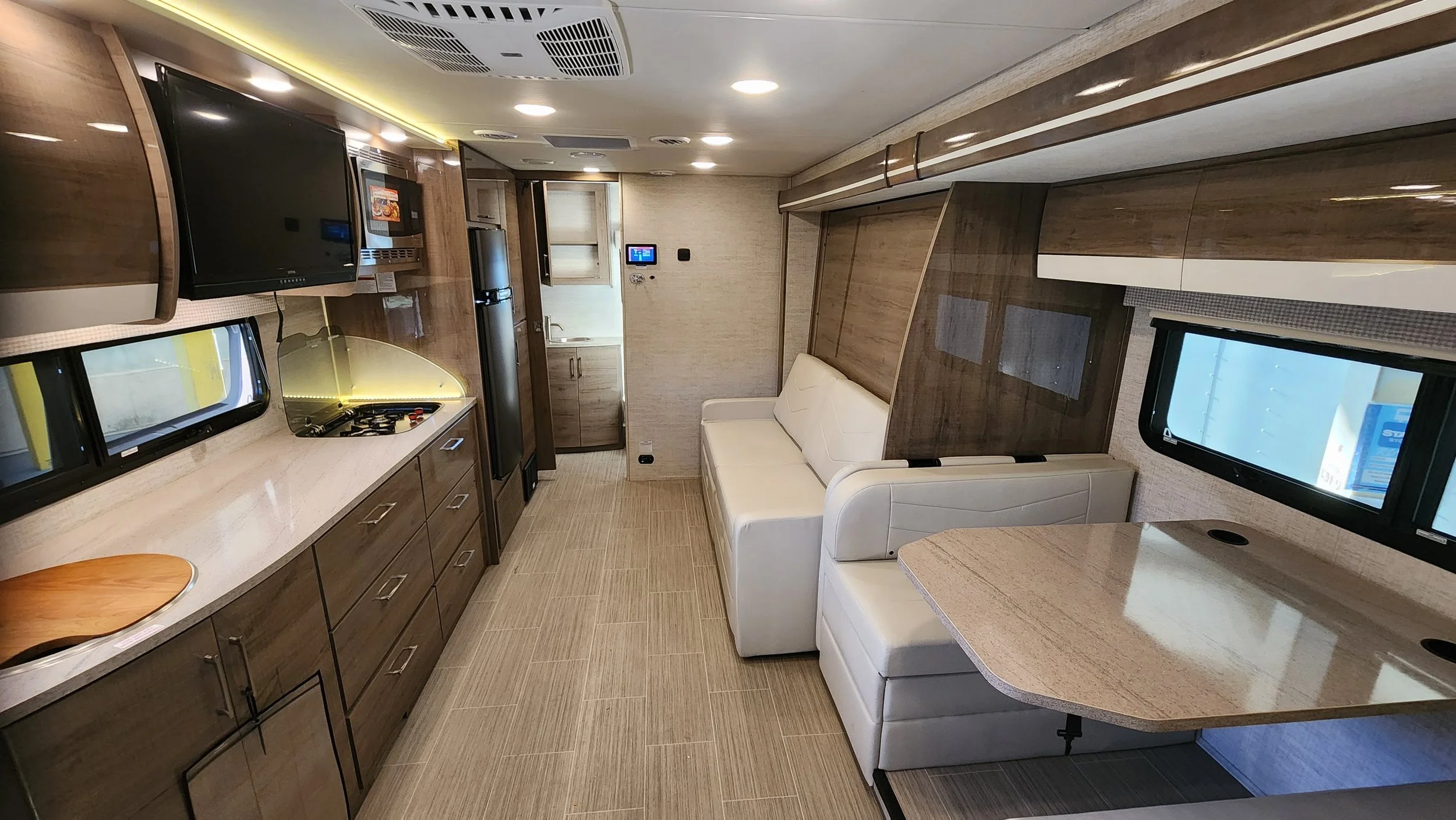 Interior of a modern recreational vehicle or camper with a kitchenette, white couch, small table, and flat-screen TV.