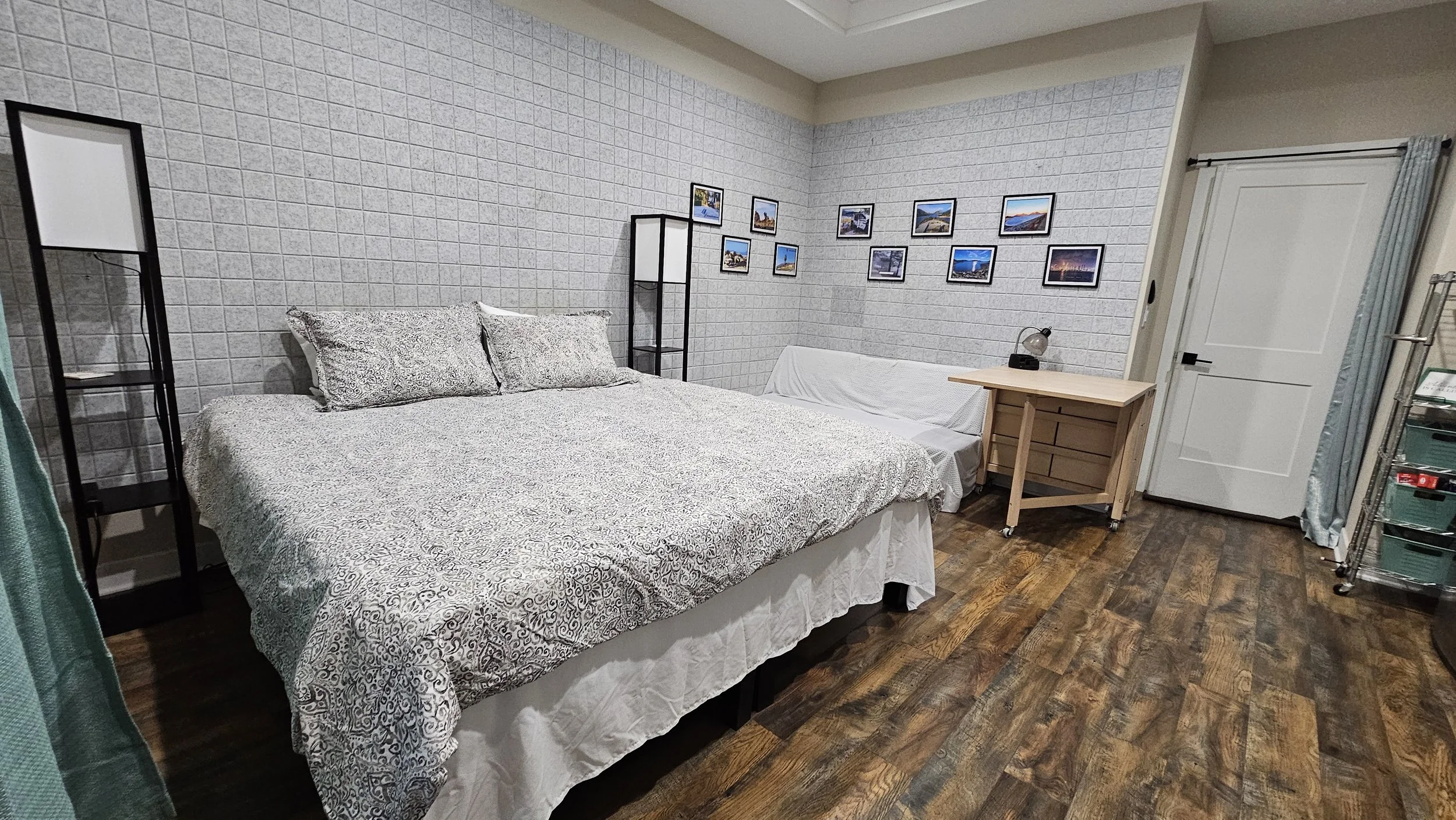 Bedroom with a large bed, a small wooden desk, and a wall decorated with framed landscape photographs.