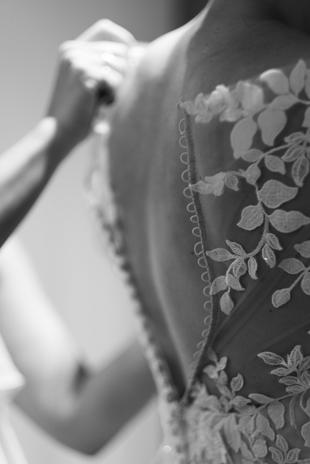 Close-up of a person adjusting a lace wedding dress with floral embroidery.