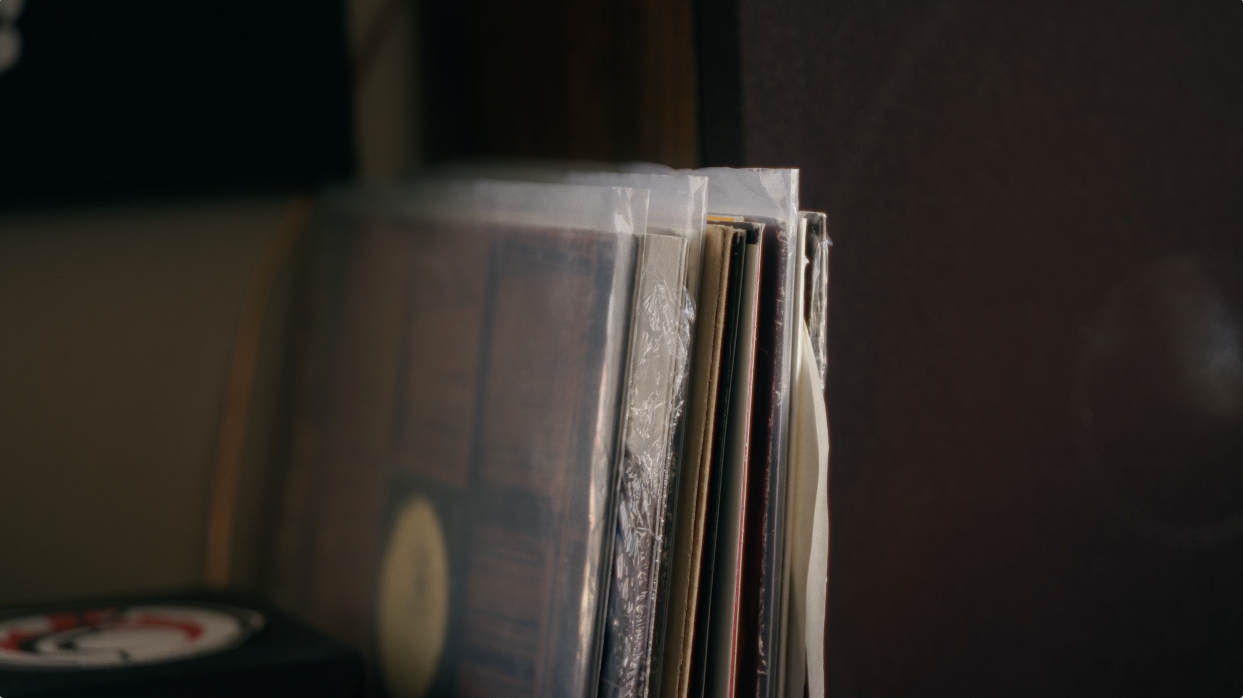 Stack of vinyl record sleeves in plastic covers on a shelf.