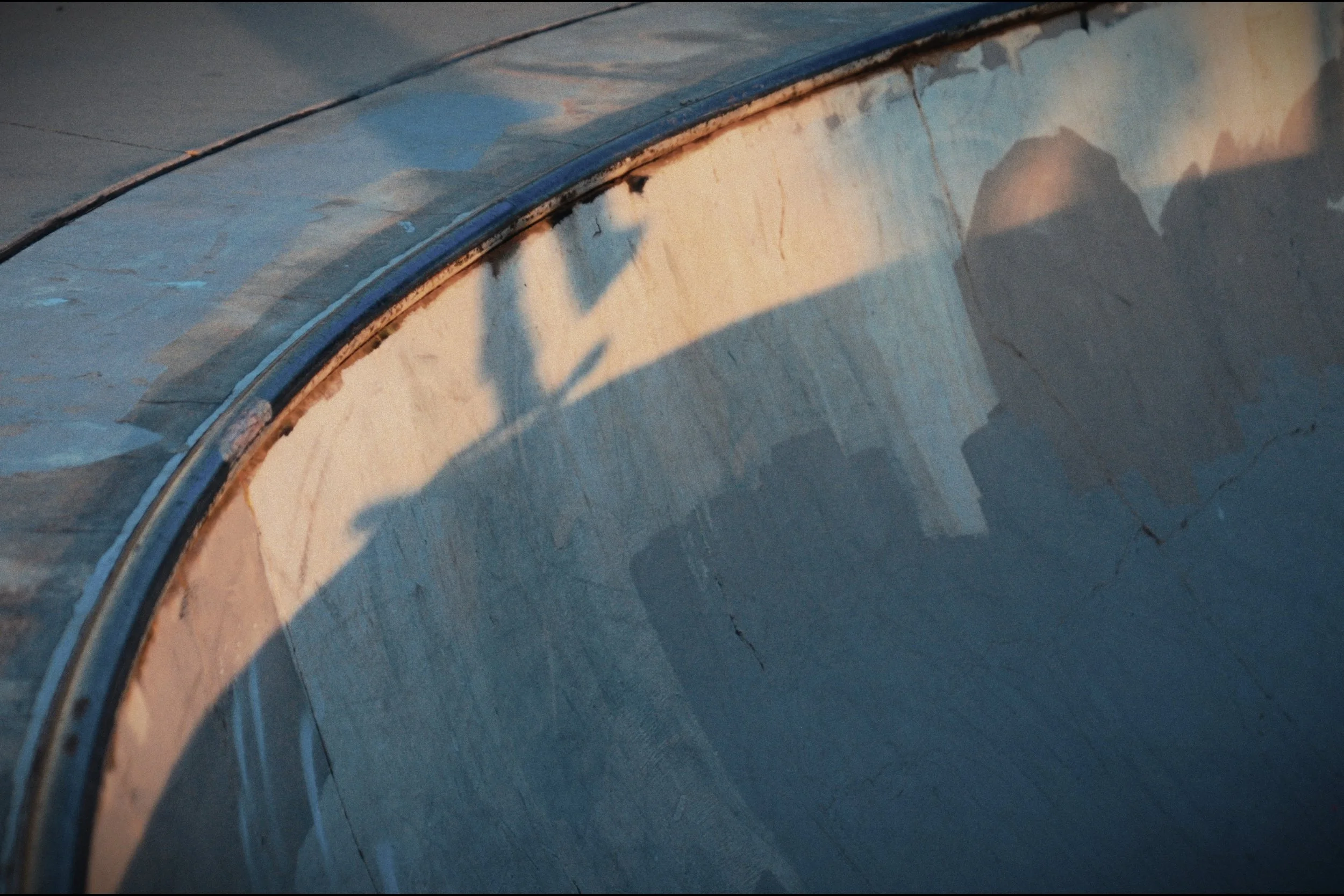 Shadow of a skateboarder on a skatepark bowl at sunset.