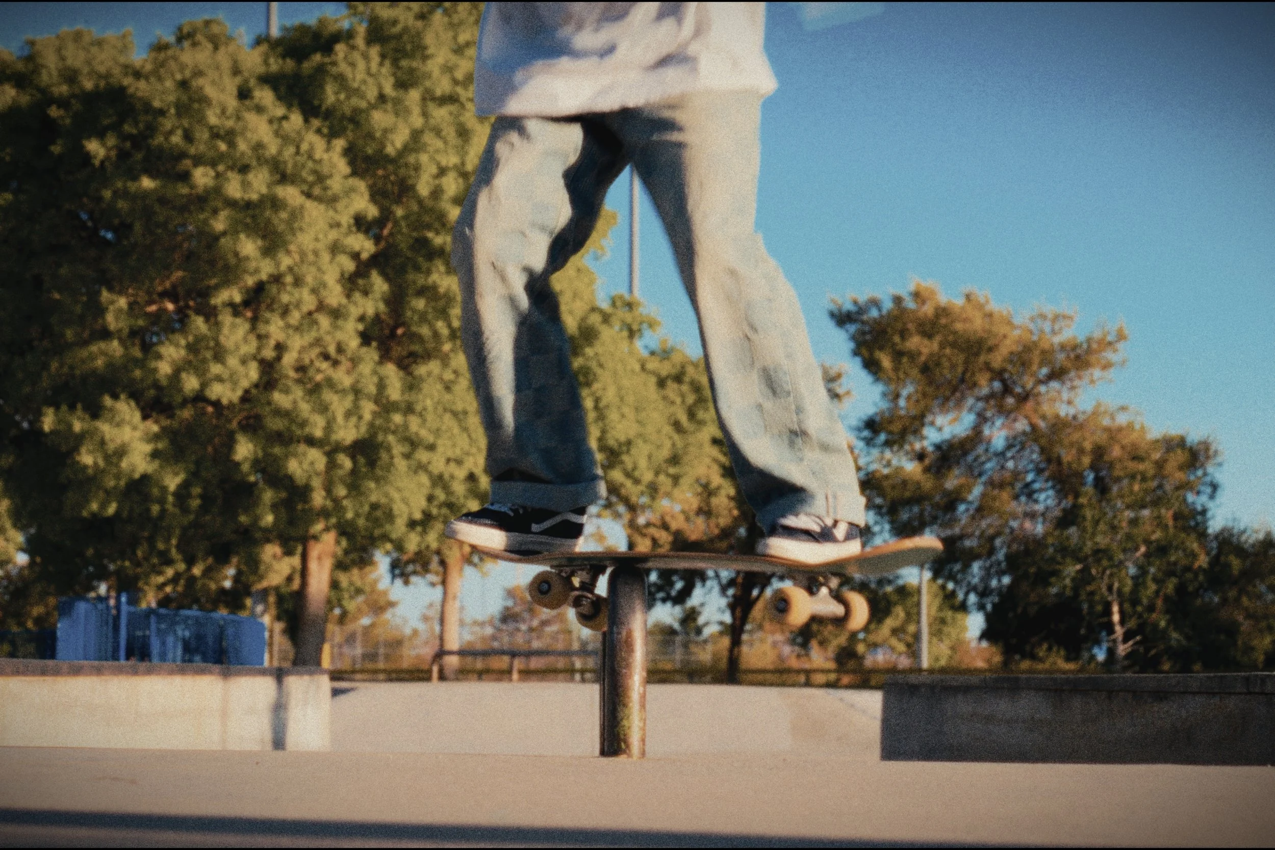 Skateboarder performing a grind trick on a rail at a skate park.