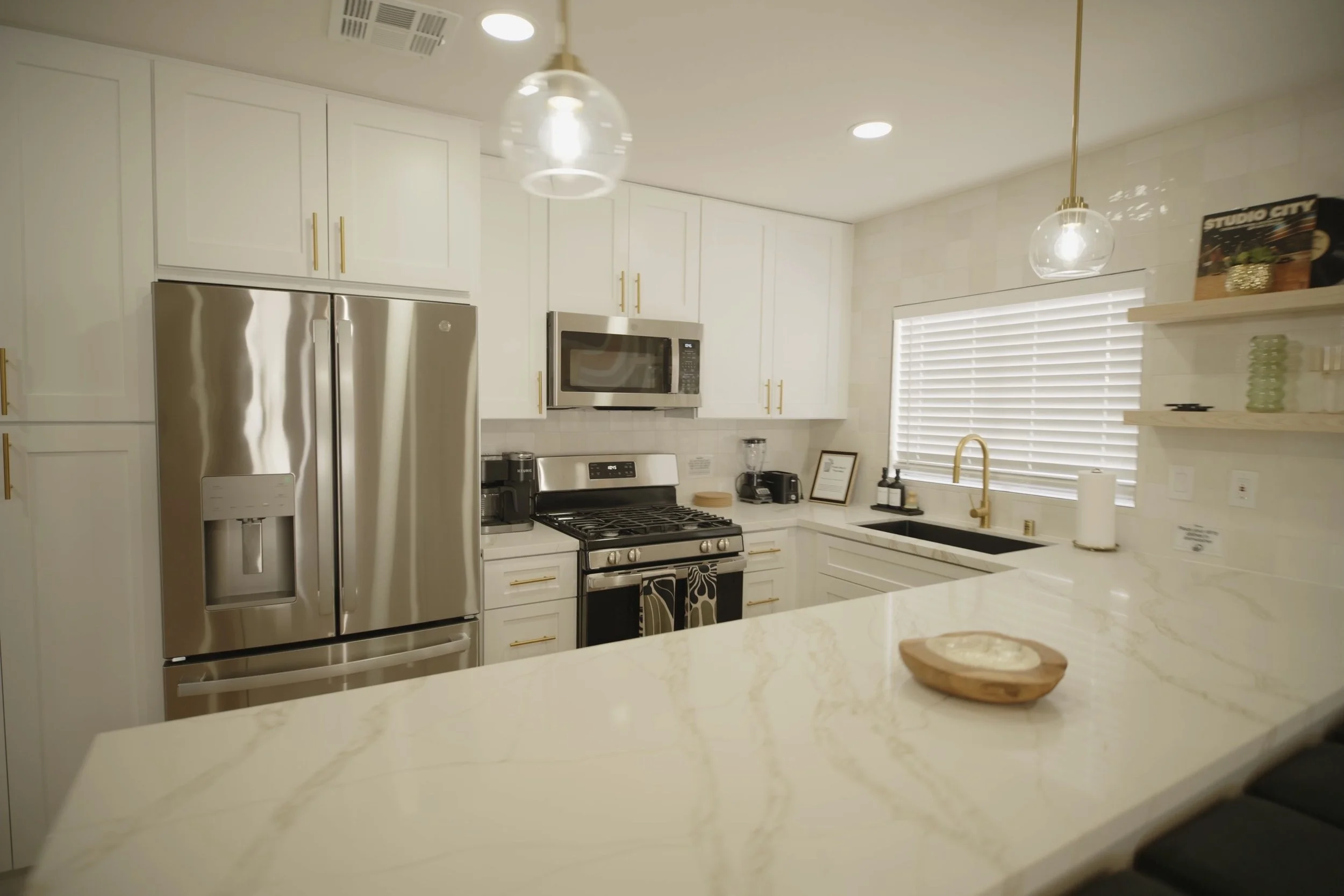 Modern kitchen with white cabinets, stainless steel appliances, marble countertops, and gold accents. Real Estate videography.