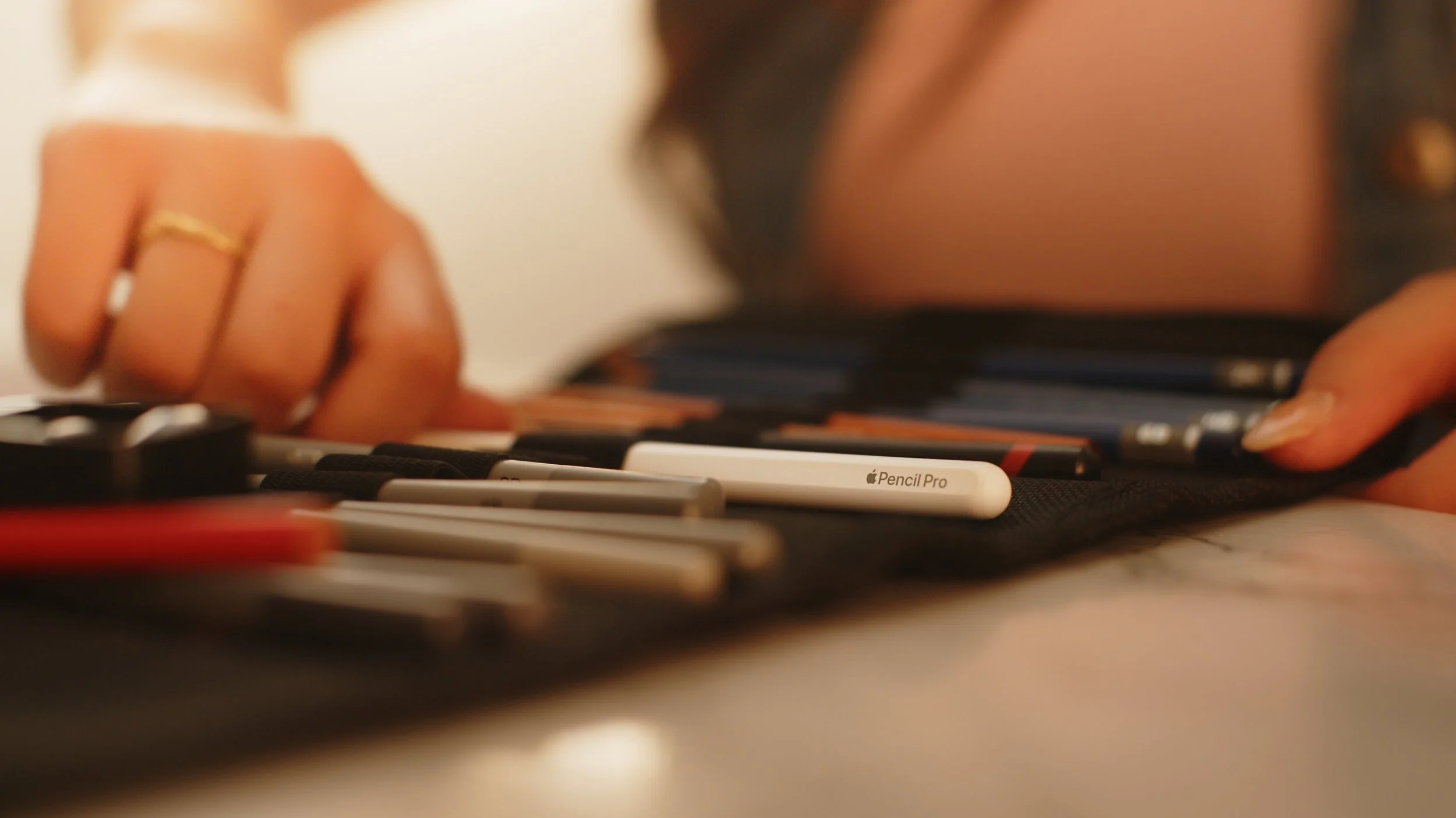Close-up of a hand organizing pencils and drawing tools, including an Apple Pencil Pro, in a case.