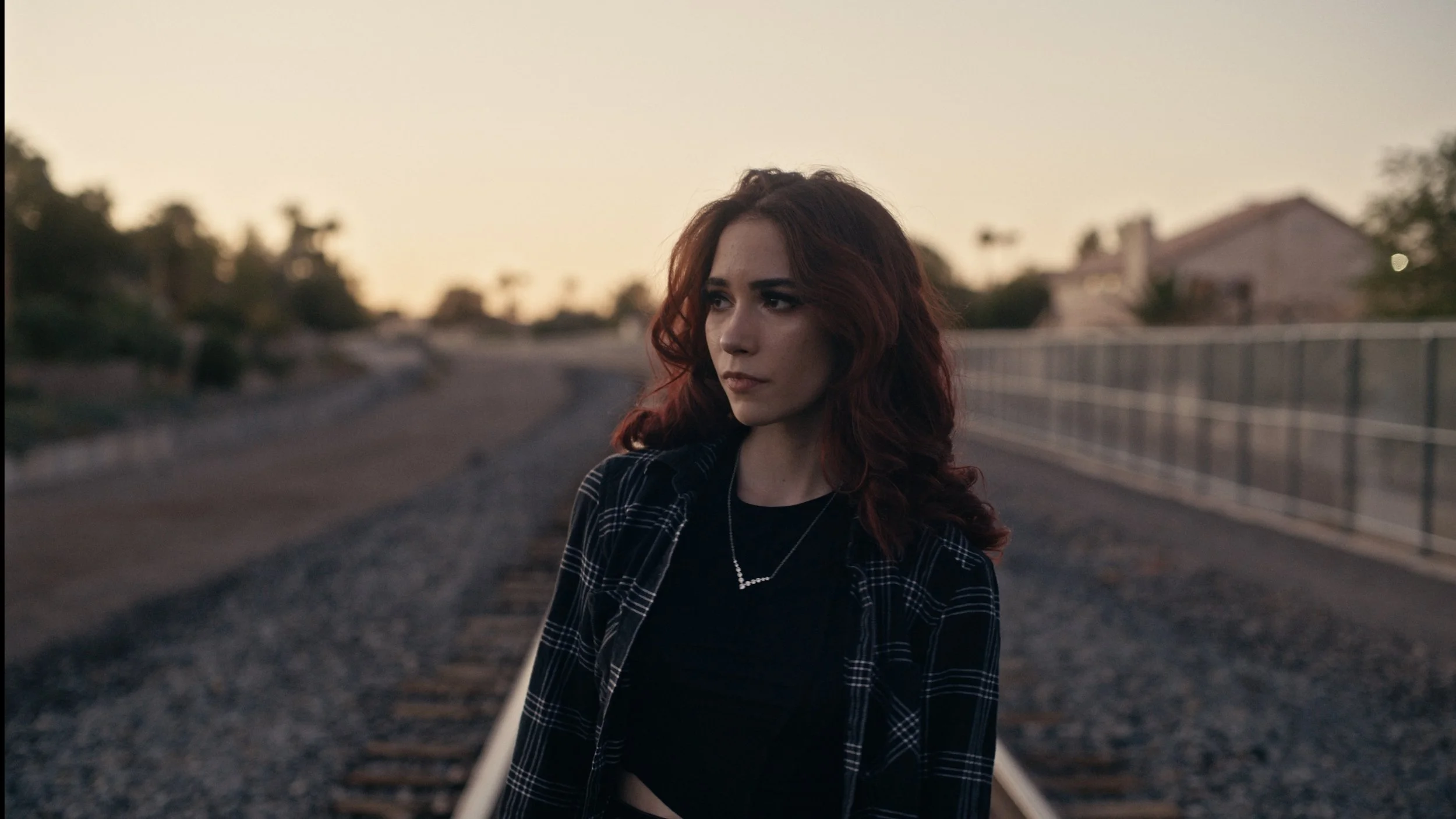 Person with red hair standing on a railroad track at sunset.
