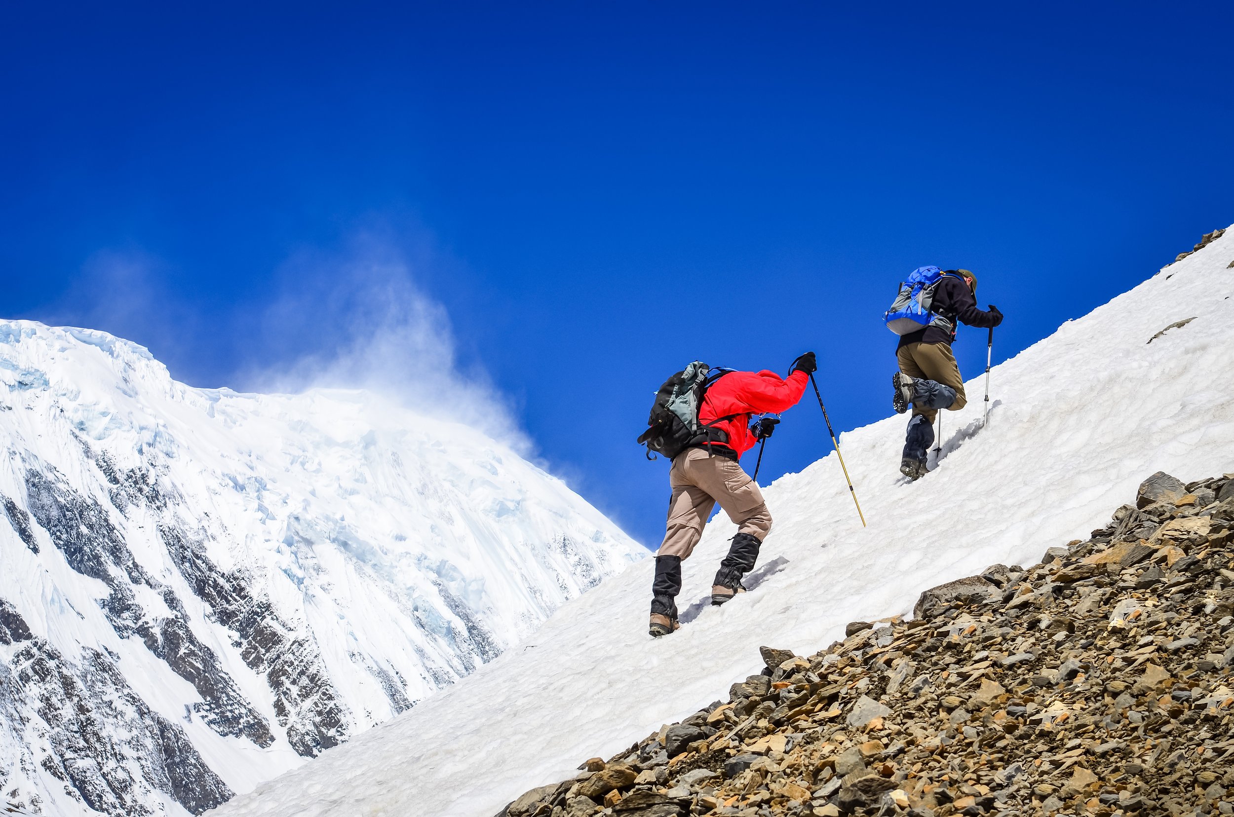 Two mountain backpackers walking on snow with peaks background, Himalayas