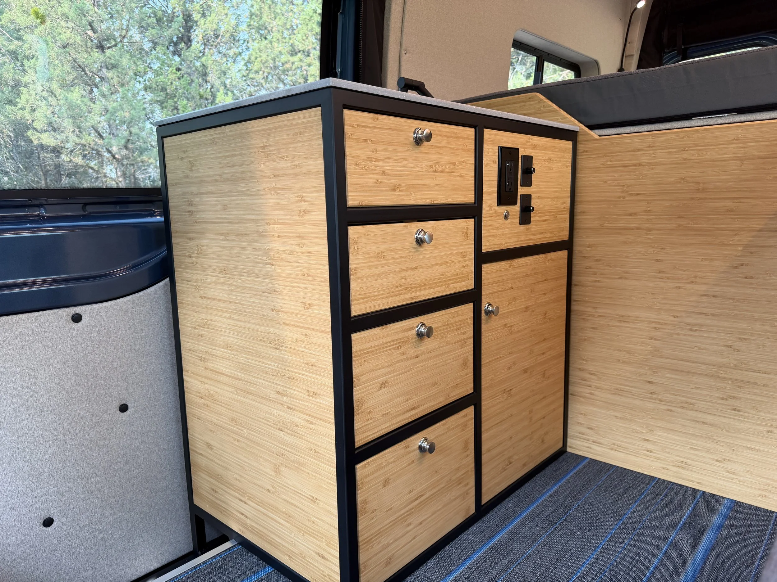 Interior of a vehicle with a wooden cabinet and a window showing trees outside.