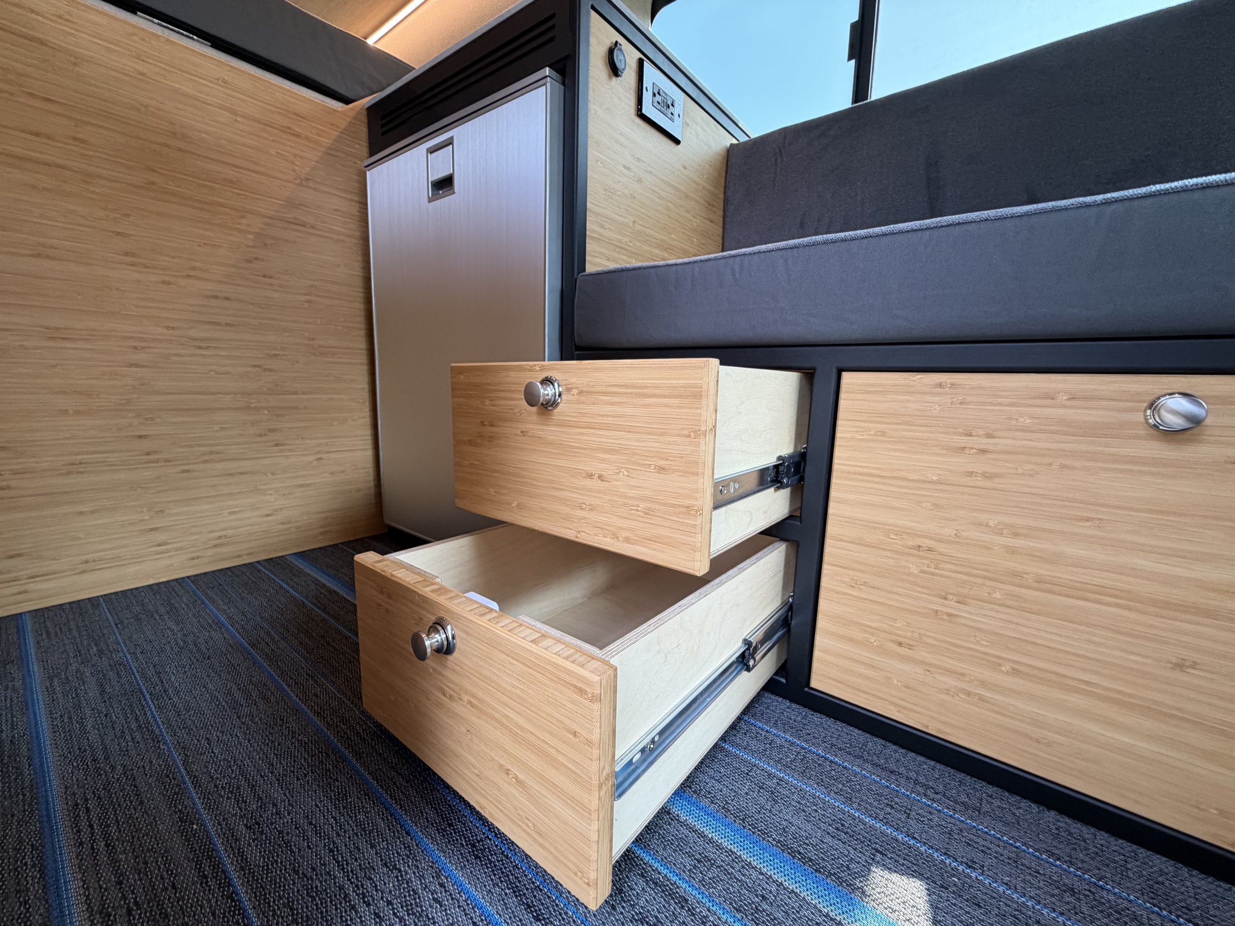 Open wooden drawers in a hotel room with a gray sofa and large window in the background.
