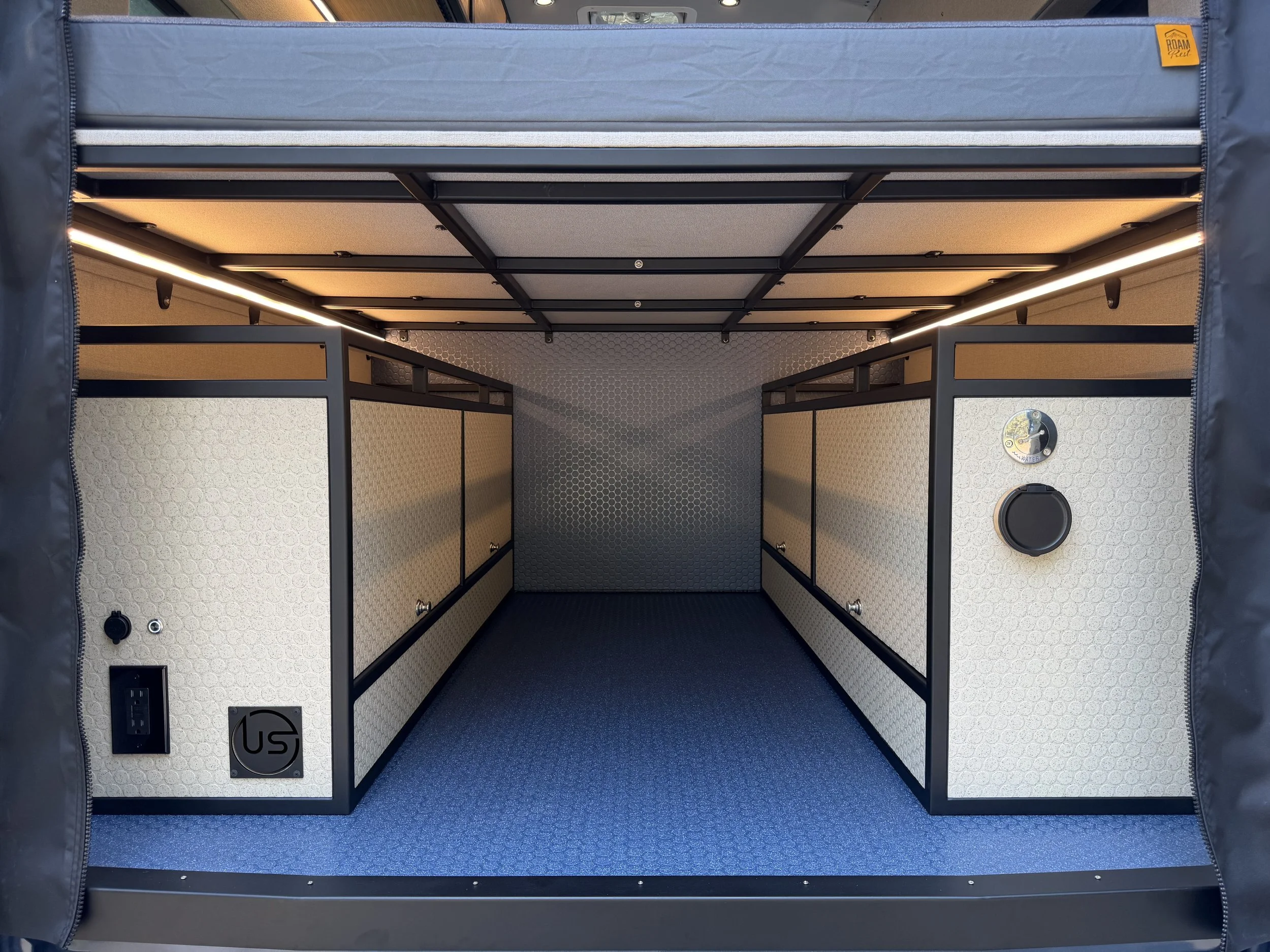 Interior of a metallic storage or work enclosure with beige fabric walls, black framing, LED lighting, two power outlets, and a small circular vent.