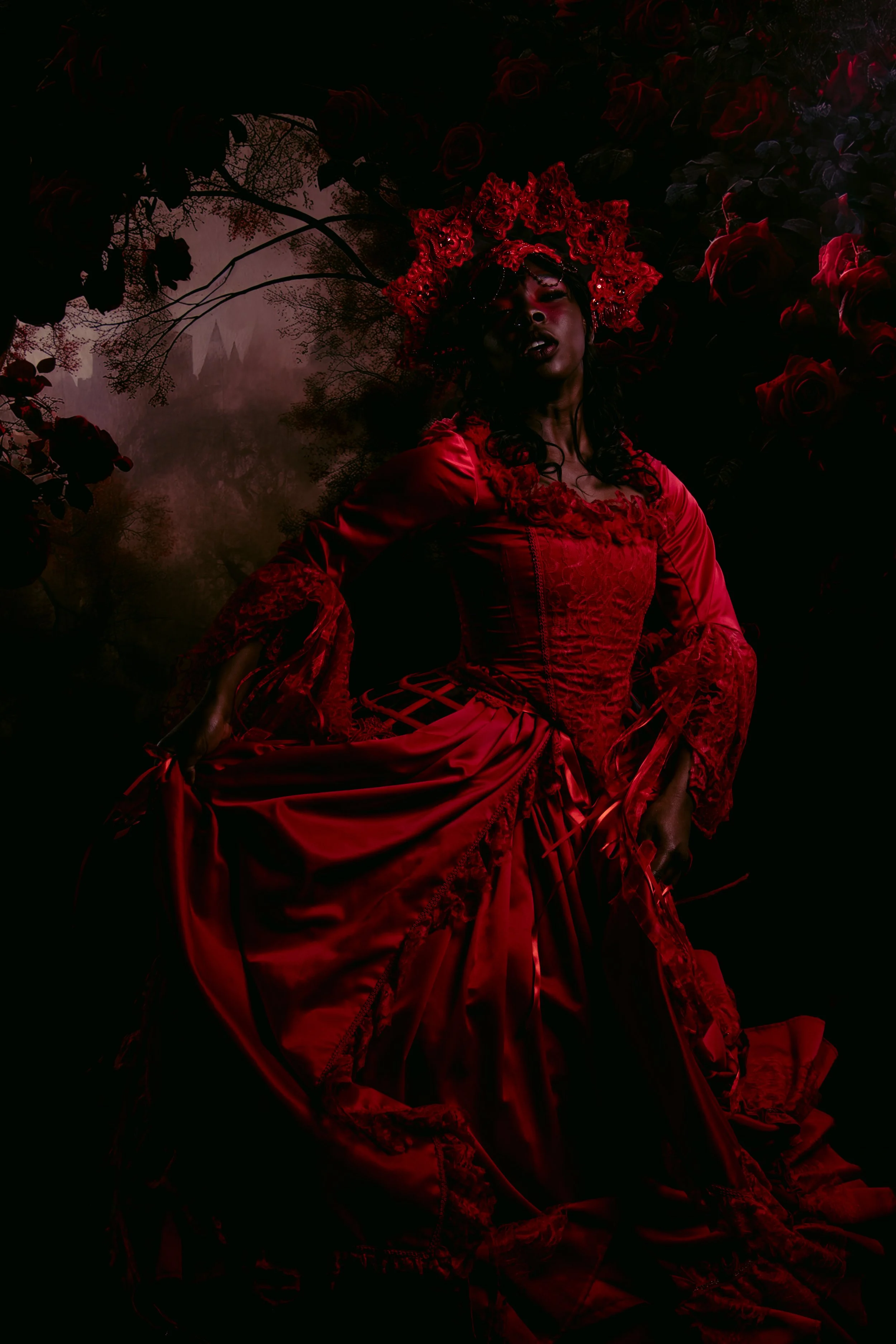 A woman in a red Victorian-style dress and floral headpiece lying among dark roses.