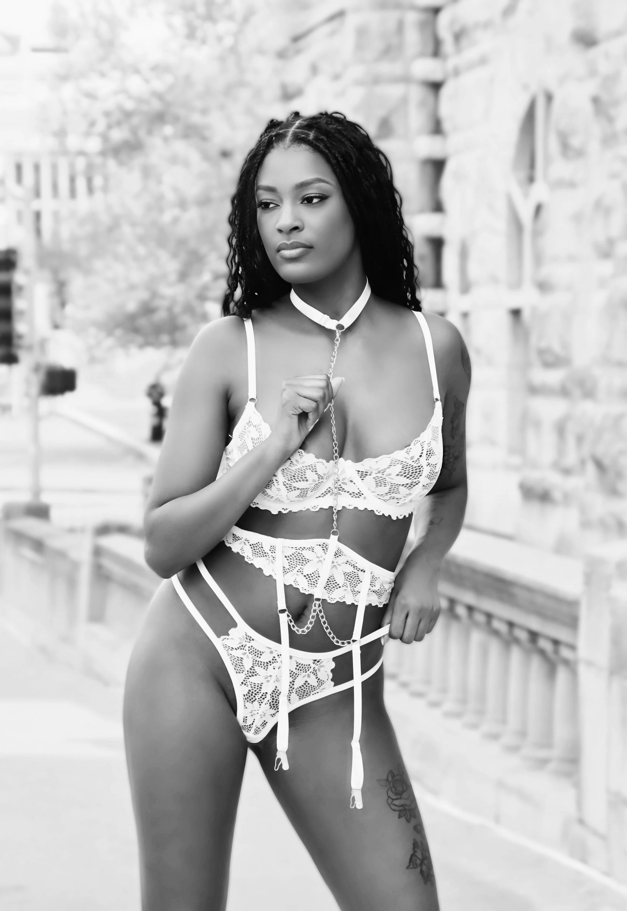 A woman wearing lace lingerie and accessories, standing outdoors with a stone building in the background.