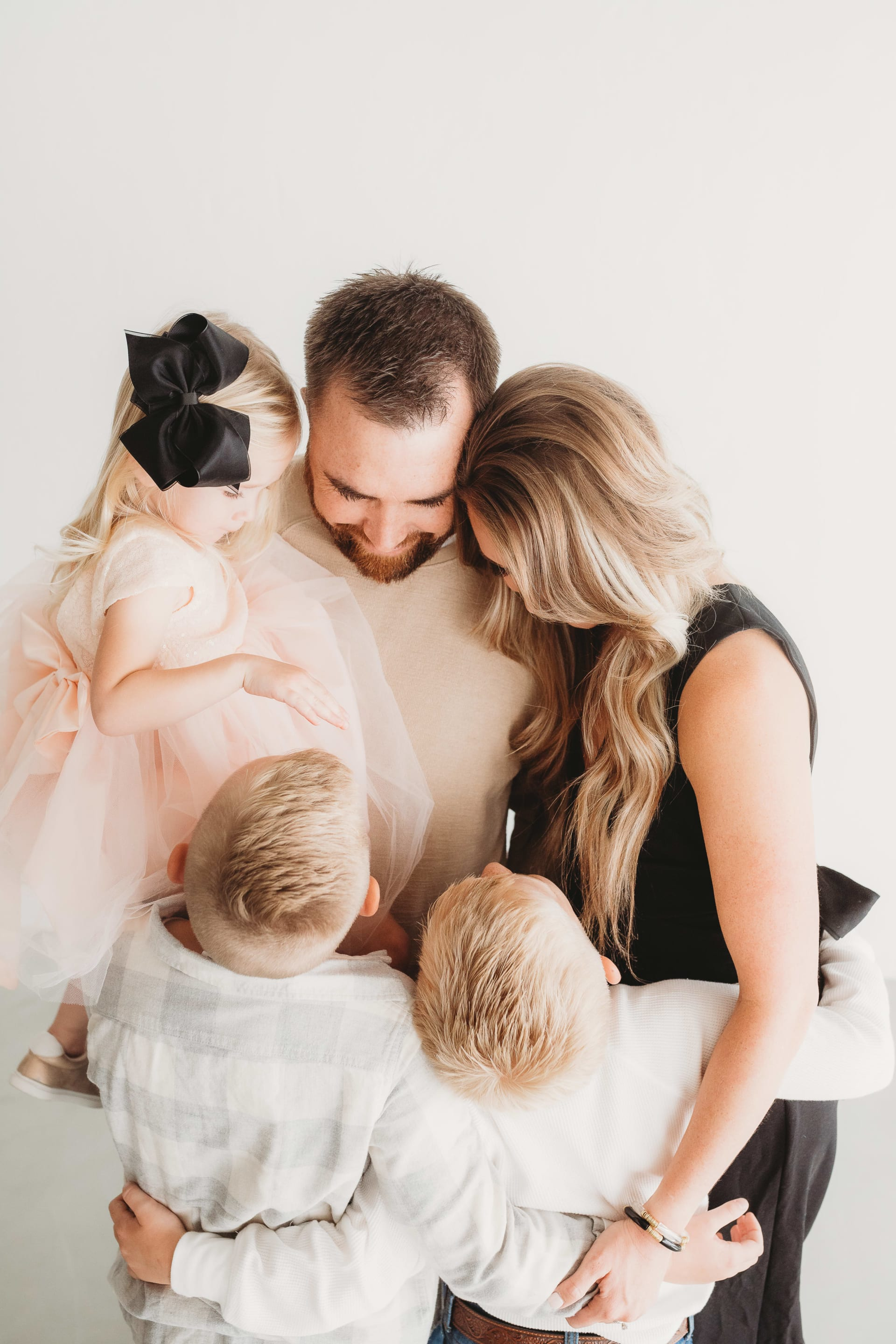 A family of five embracing, including two adults and three children dressed in coordinated attire, with light background.