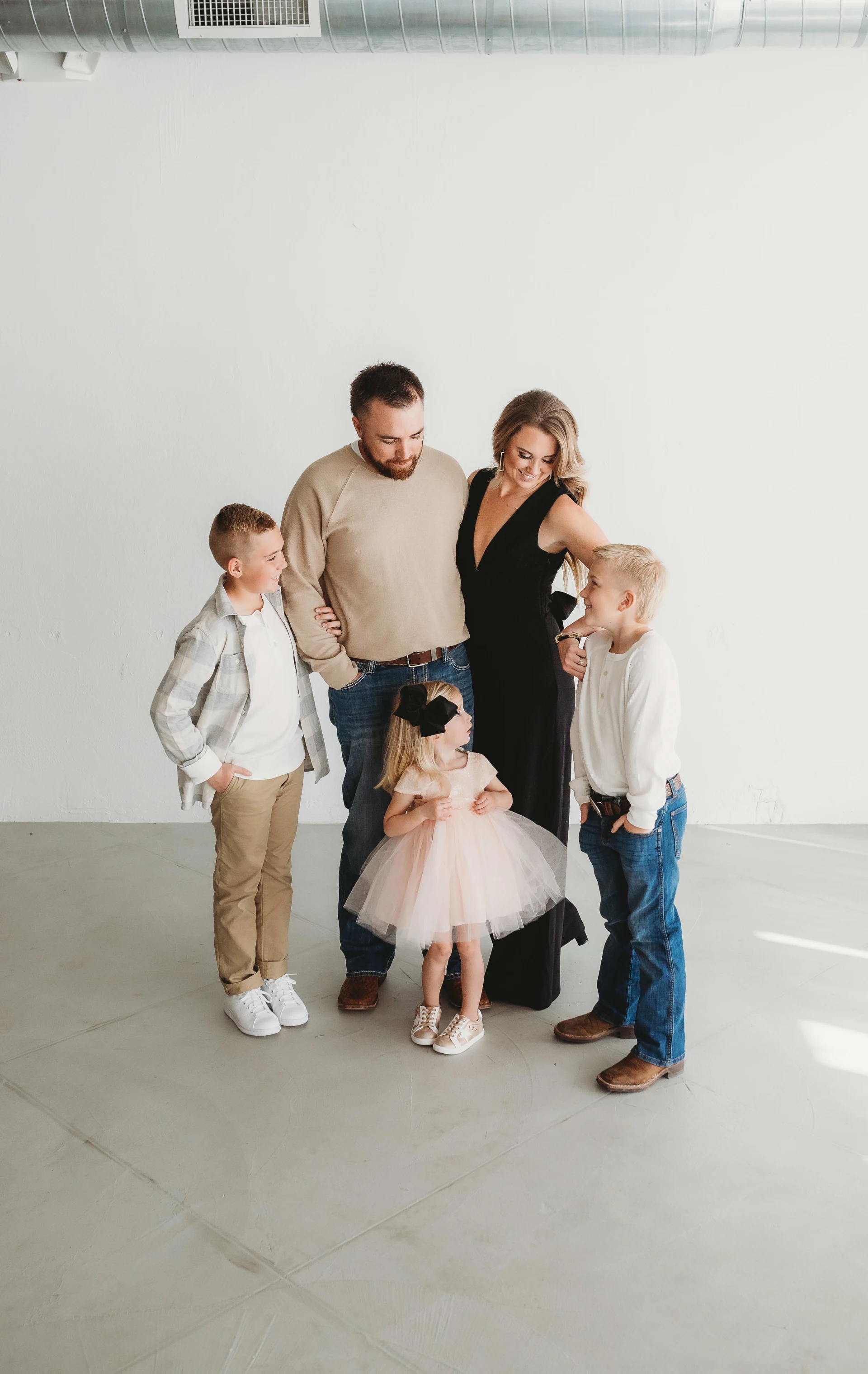 Family portrait with a mother, father, three children; two boys and a girl in a dress, posing indoors.