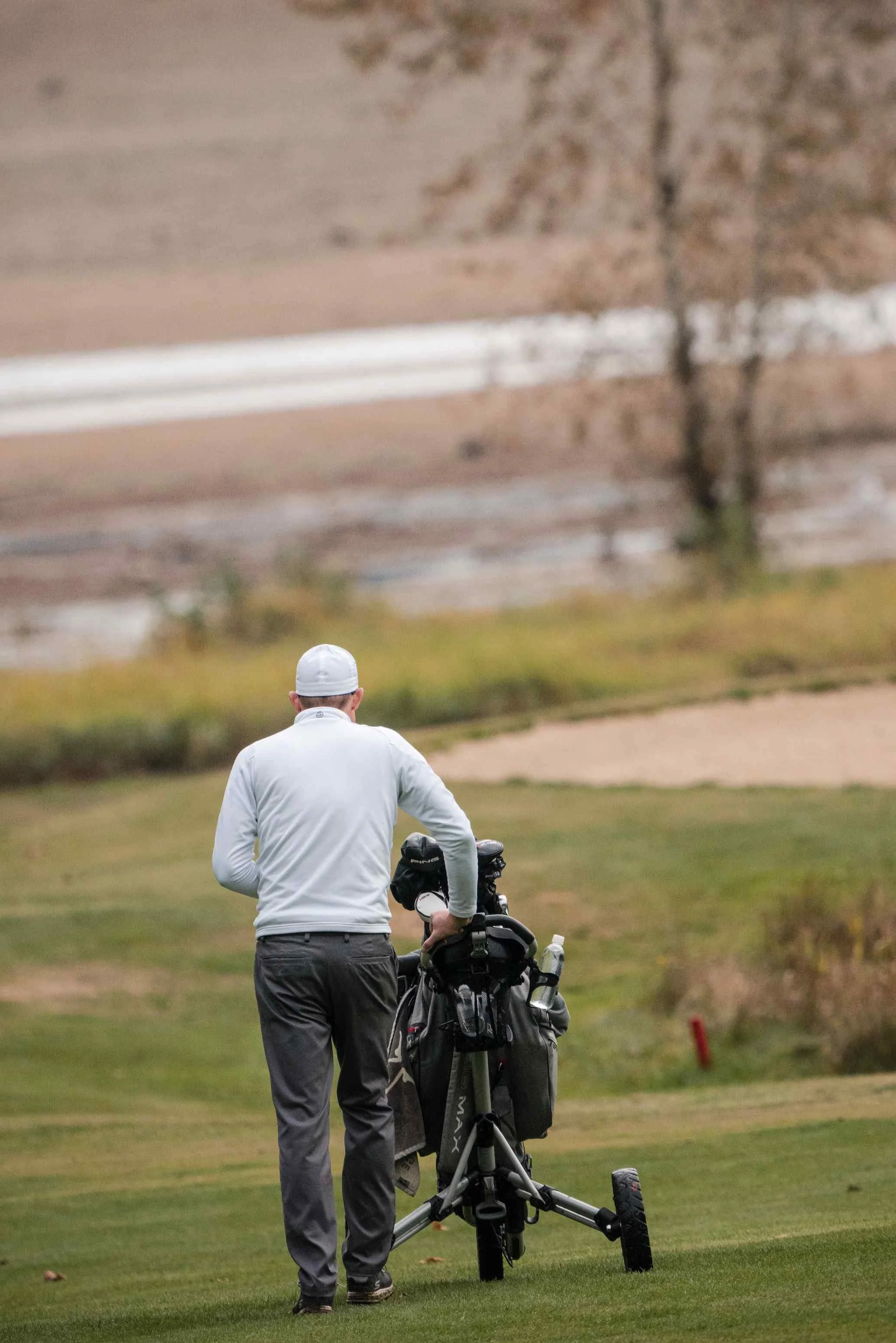 Golfer pushing a push cart down an autumn fairway near a sand bunker in a golf course community.
