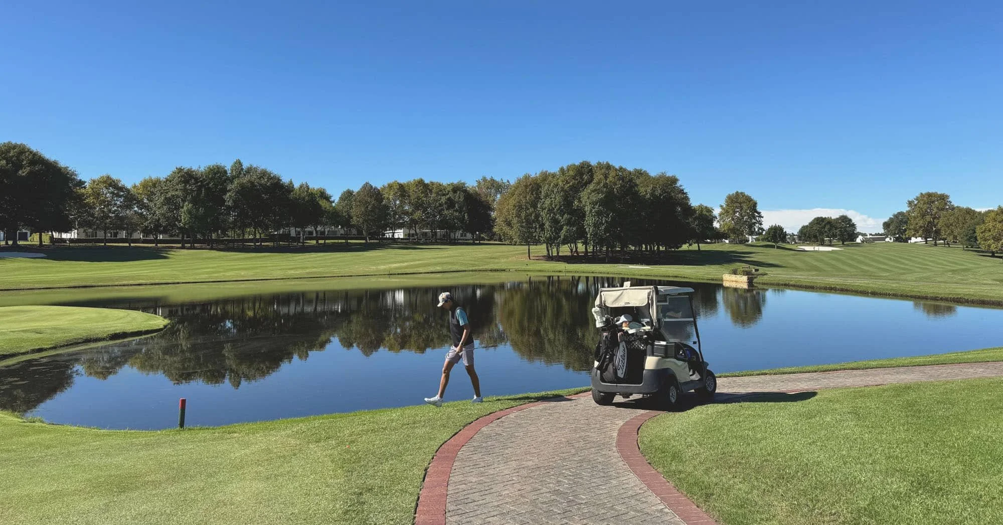 Golfer walking a cart path beside a pond on a Kansas City golf course community, golf cart parked nearby