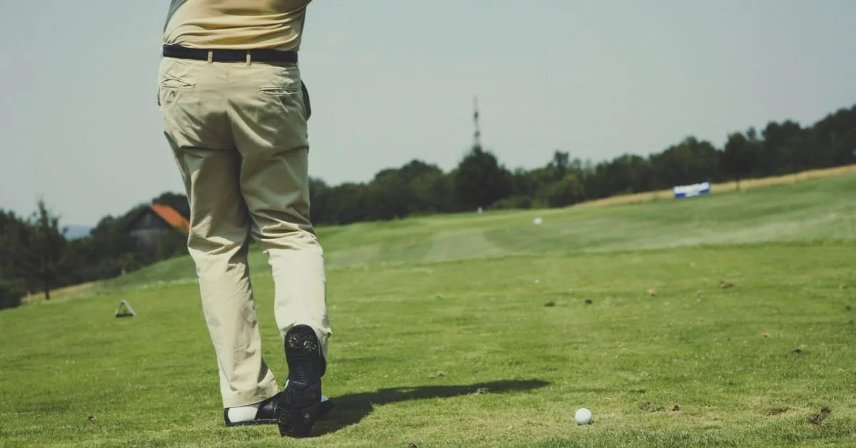 Golfer in khaki pants follows through on a swing across a green fairway in a Kansas City golf course community.