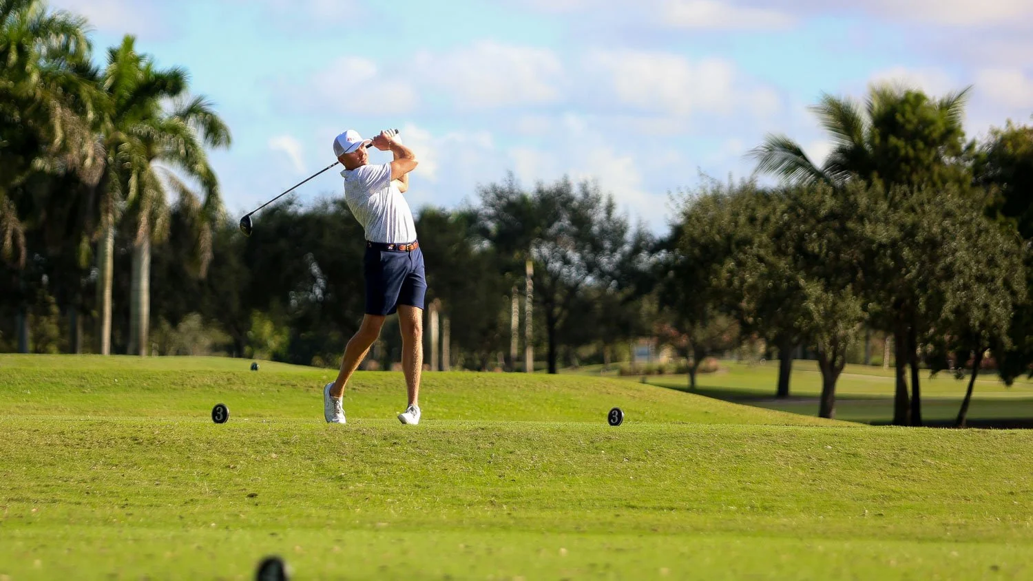 Golfer taking a swing at one of the best golf courses in Kansas City, with lush palm-lined fairways in the background.