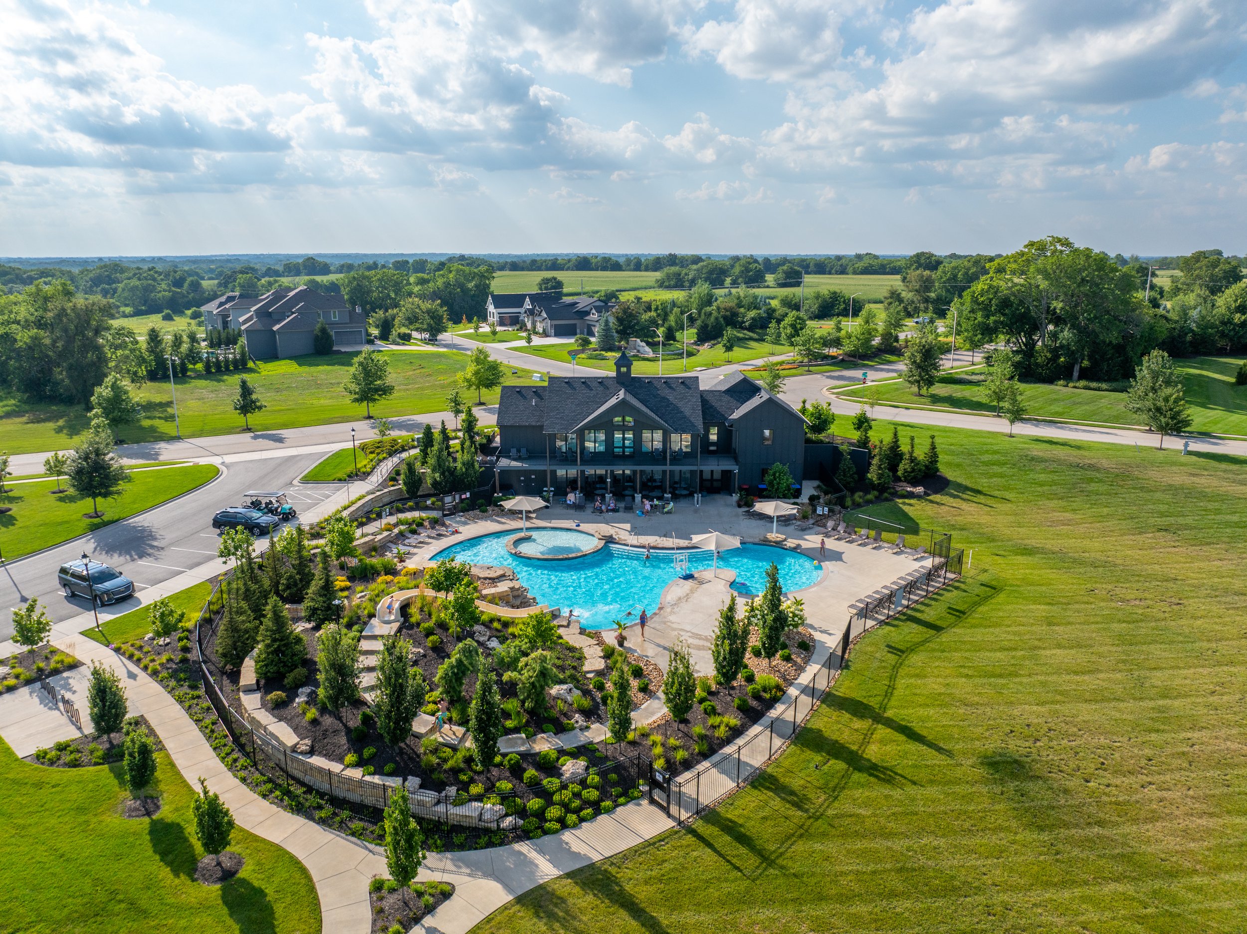Aerial view of a neighborhood clubhouse and resort-style pool with a waterslide, surrounded by landscaping and homes in South Overland Park, KS