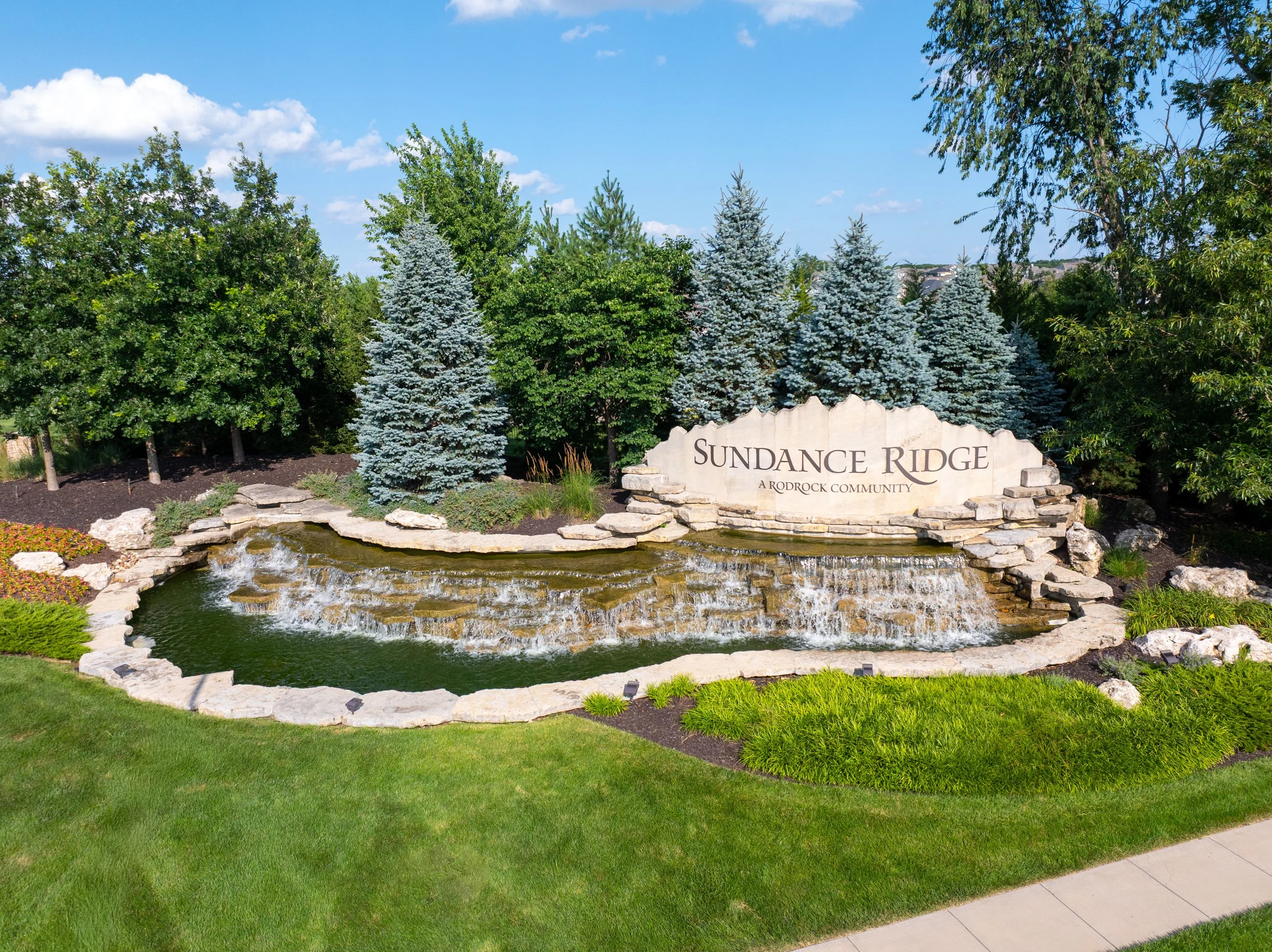 Stone entrance monument for Sundance Ridge, a Rodrock community in Overland Park, KS, with a cascading waterfall and evergreen trees