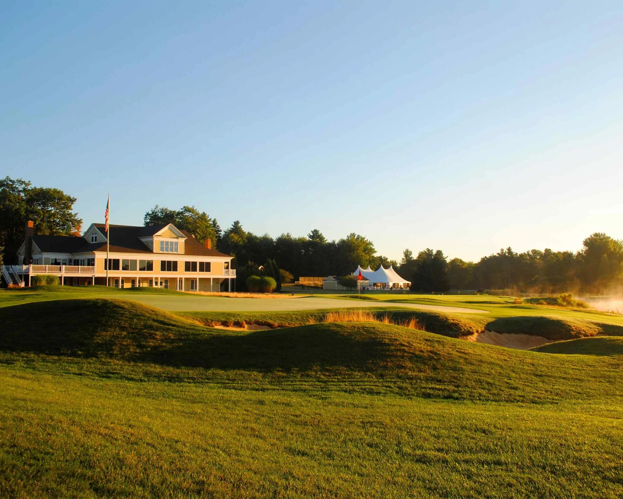 Sunrise view of a golf course green with sand bunkers and clubhouse showing how a golf course view can add home value.