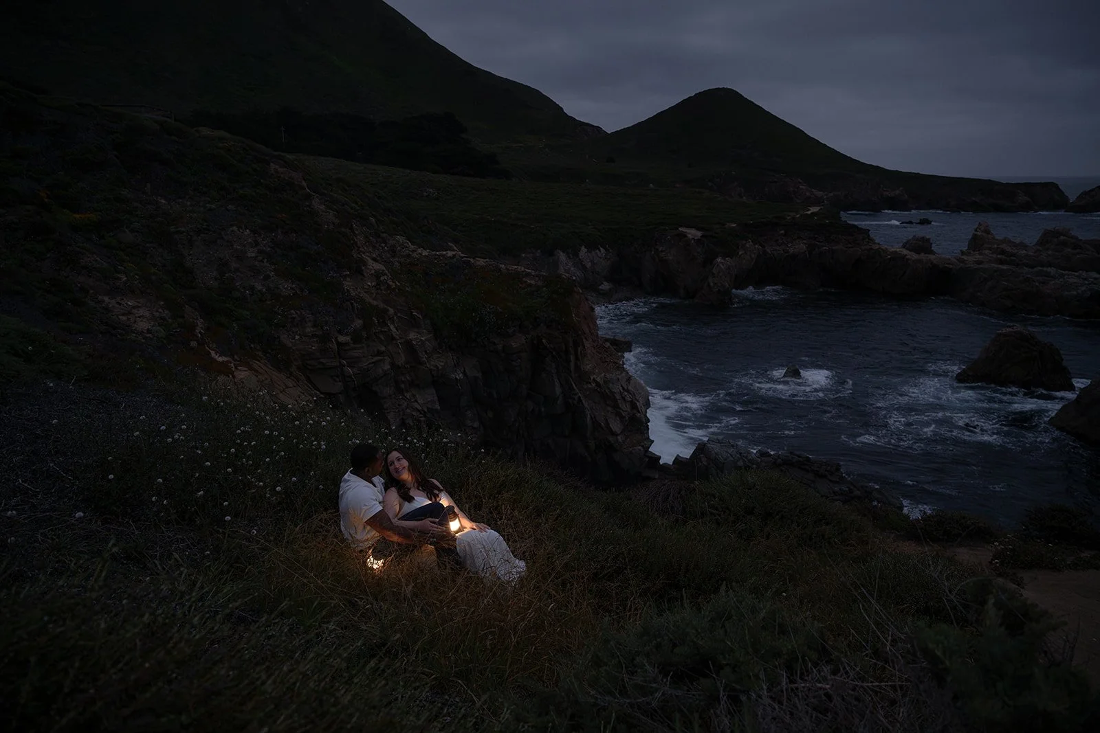 bride and groom sitting on a cliffside with lanterns