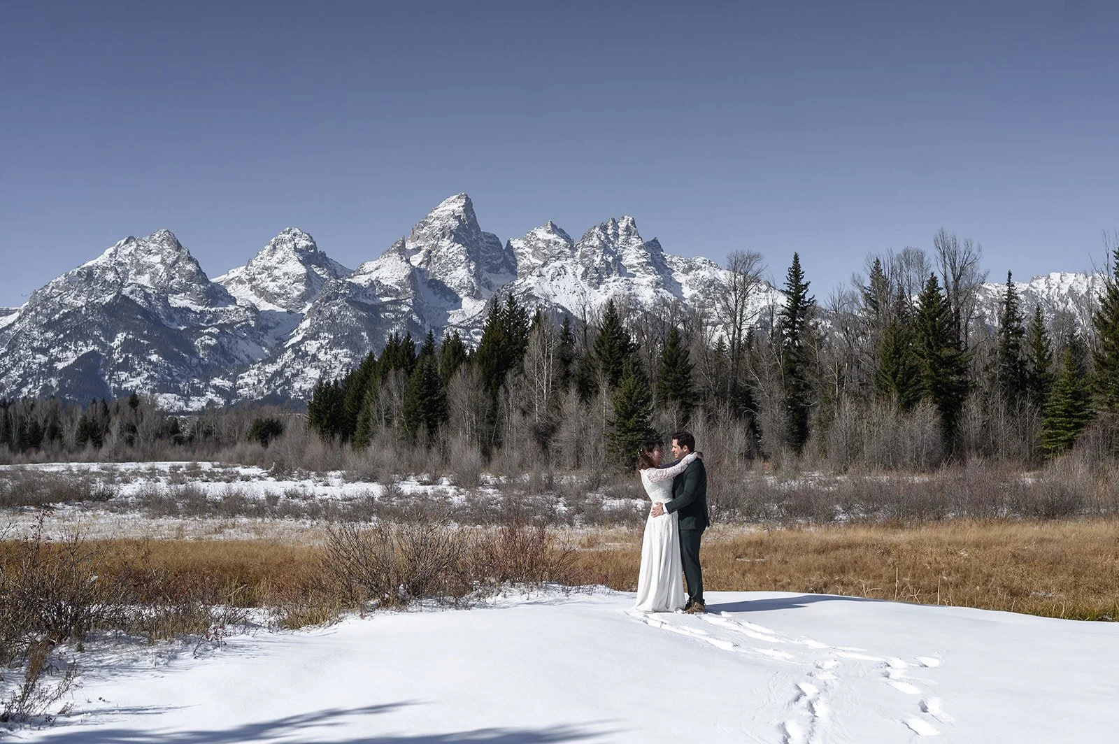a snowy adventure elopement in the grand tetons national park with the bride and groom hugging each other in the snow with the grand tetons mountains behind them