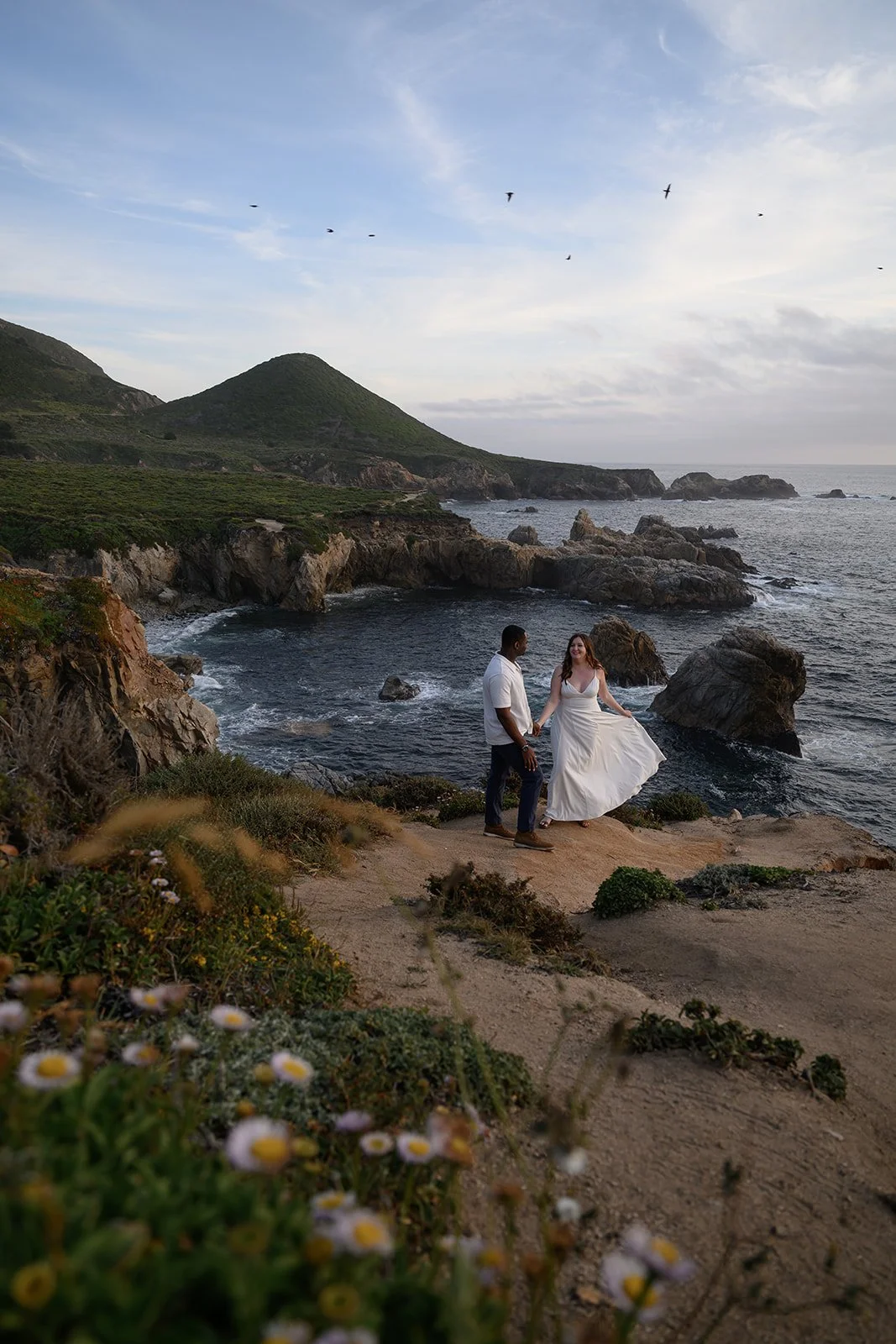 a bride and groom on a cliffside in big sur on their wedding day at sunset
