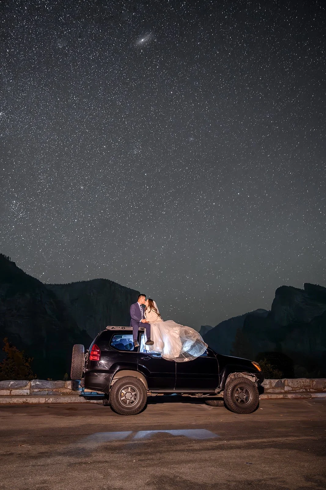 a couple on their wedding day sitting on top of a car in yosemite with a starry sky behind them