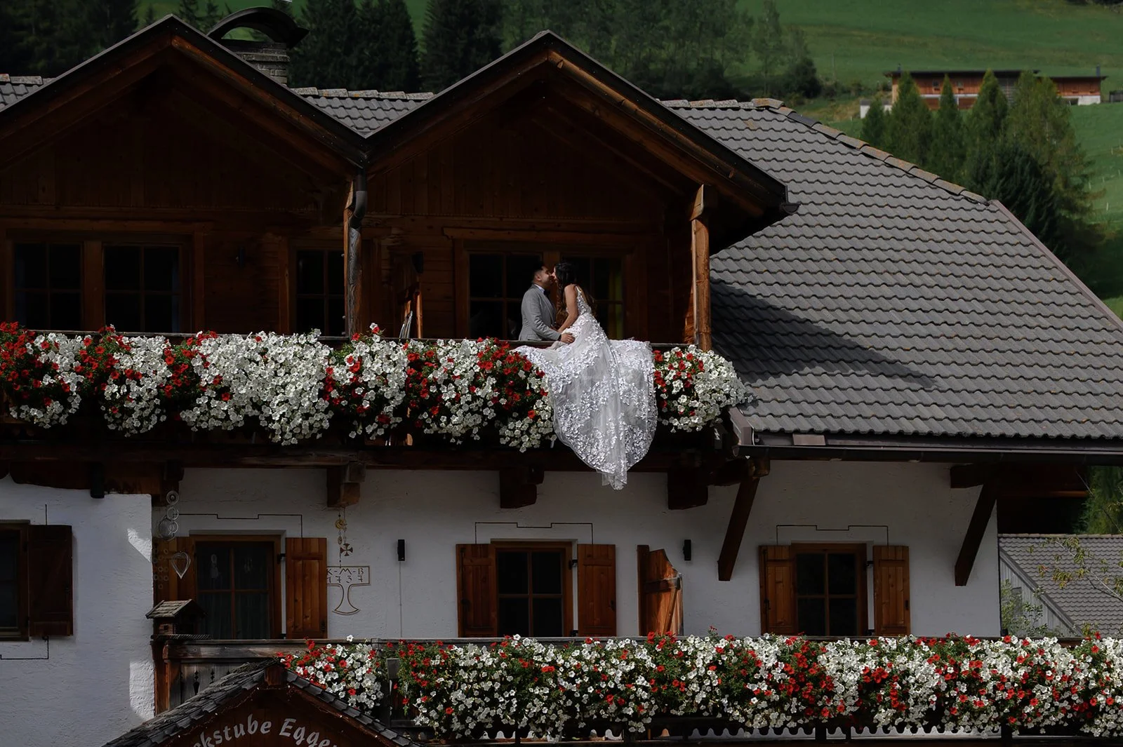 a bride and groom sitting on a balcony covered in flowers in the Dolomites in Italy on their wedding day