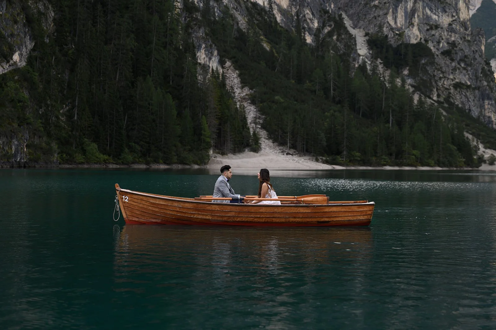 a couple sitting in row boat on a lake in their wedding attire